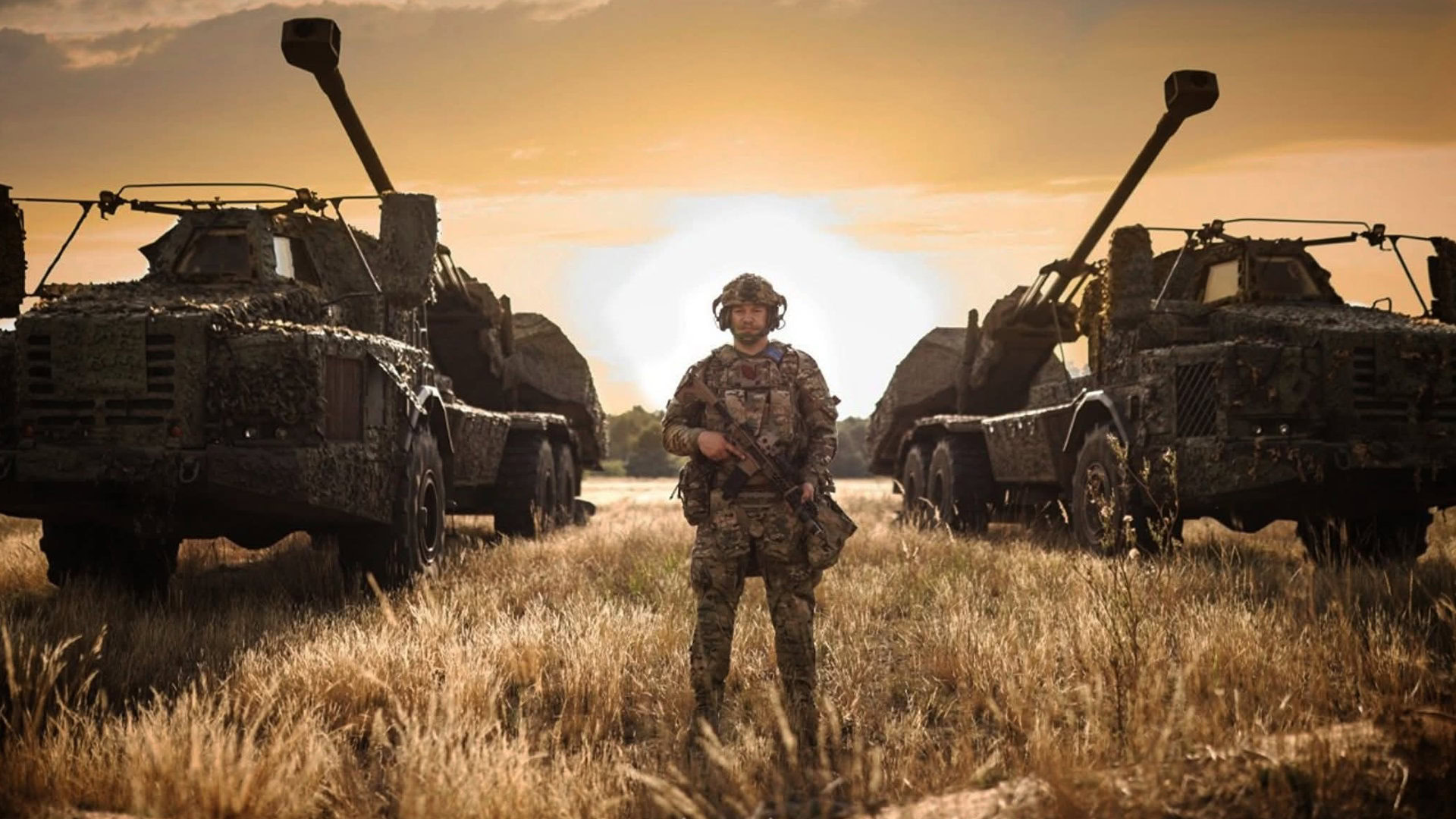 Військовий ЗСУ стоїть між двома вантажівками з гарматами