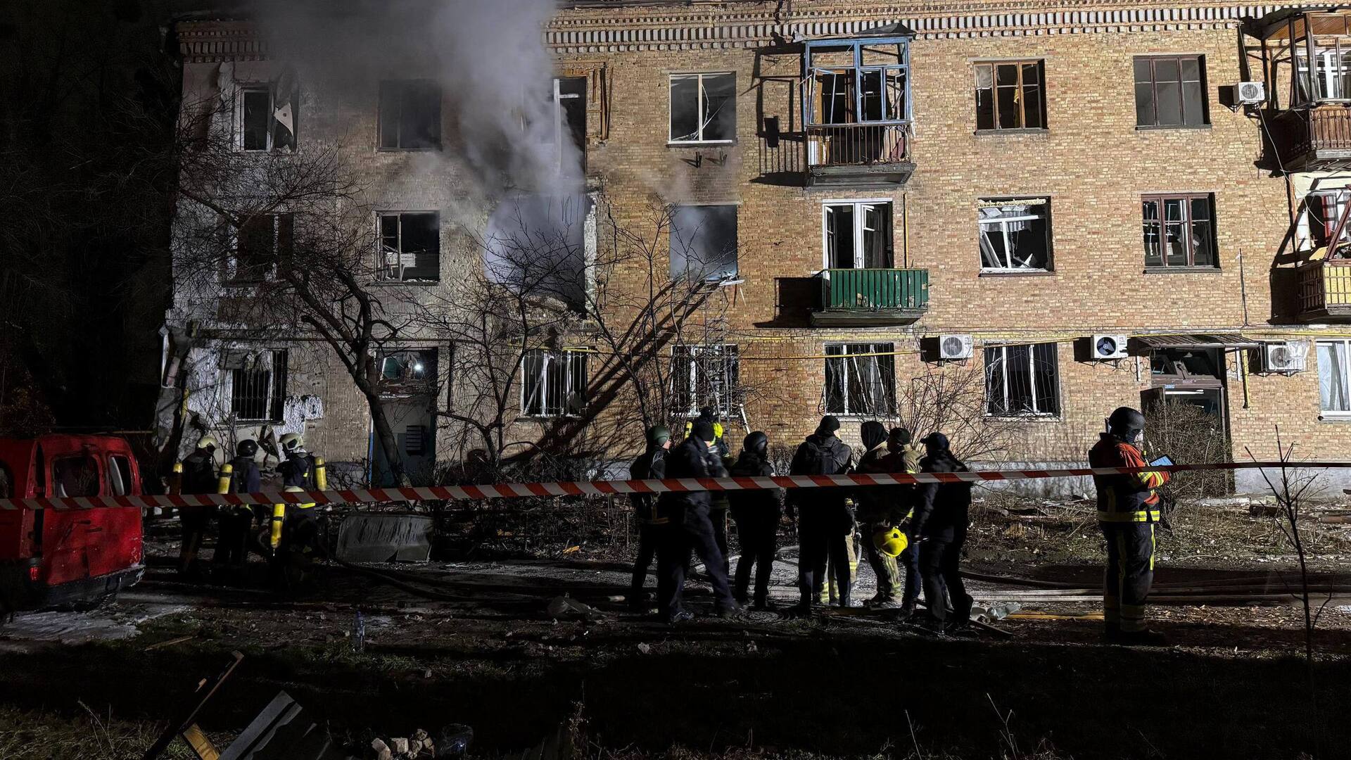 Рятувальники стоять біля житлового будинку в Києві, пошкодженого російським обстрілом. З вікон іде дим