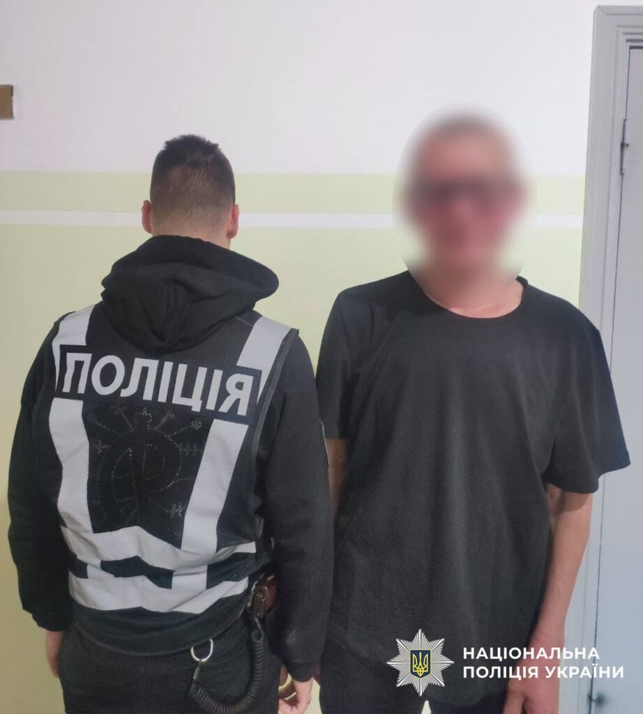 Поліейський тримає чоловіка в чорній футболці і окулярах, обличчя заблоюрене