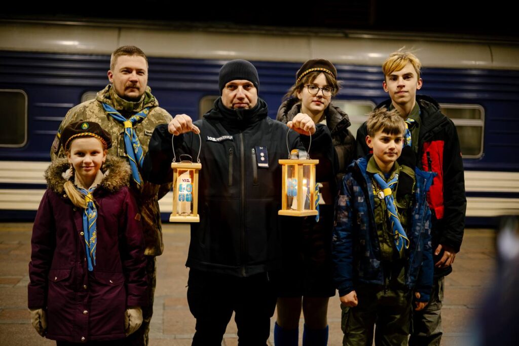 Дорослі та діти тримають свічки з Вифлеємським вогнем в руках на пероні