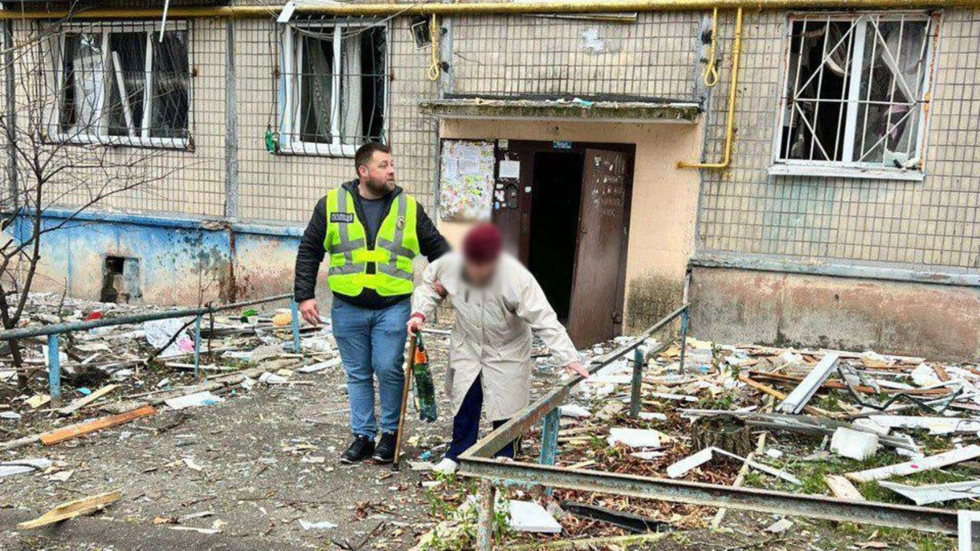 Поліцейський надає допомогу жінці похилого віку біля пошкодженого житлового будинку