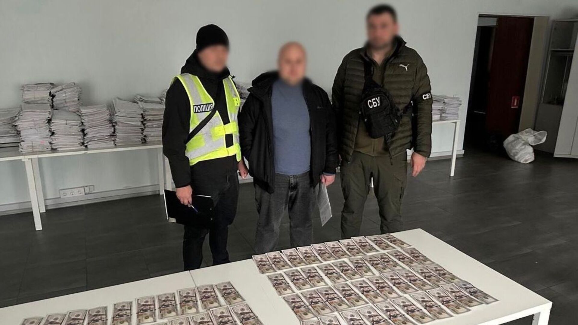 Поліцейські з затриманим біля столу, на якому розкладені купюри