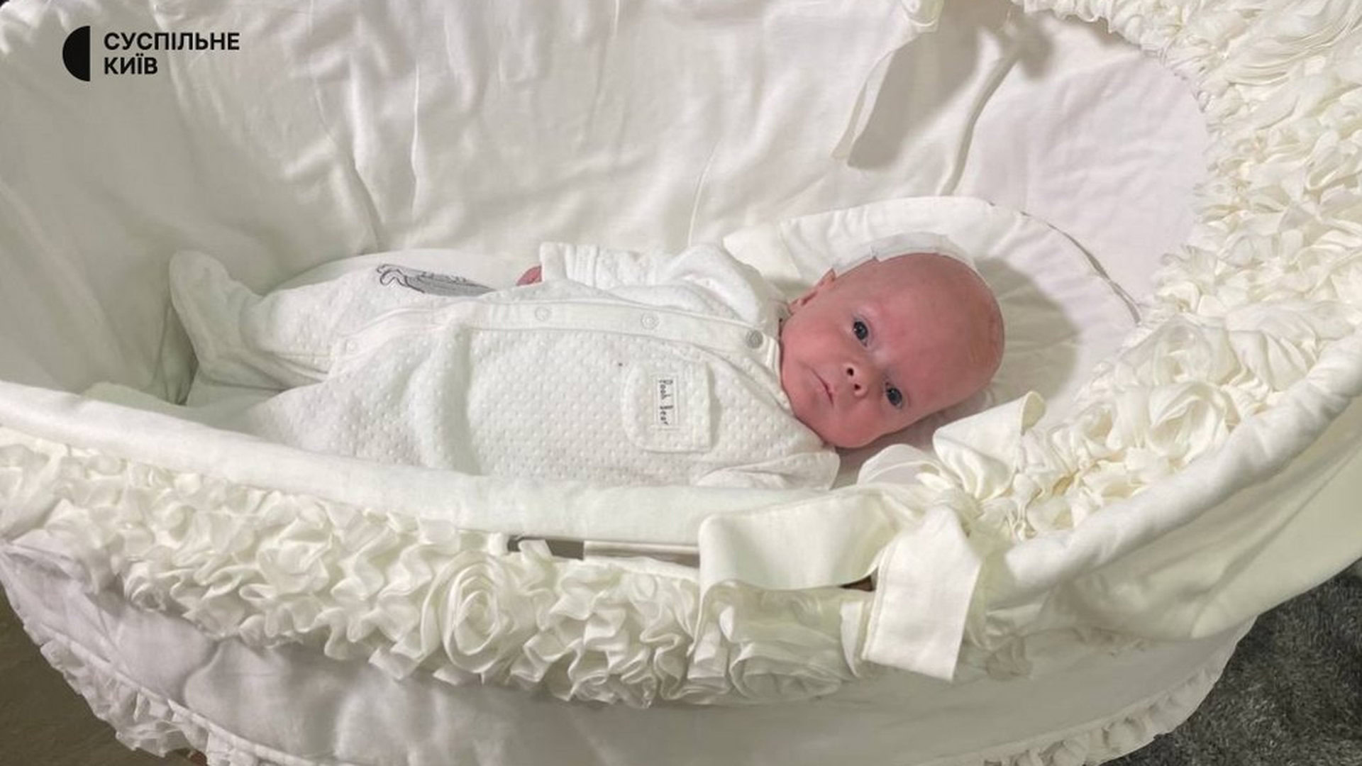 Немовля лежить в білому одязі в білій люльці