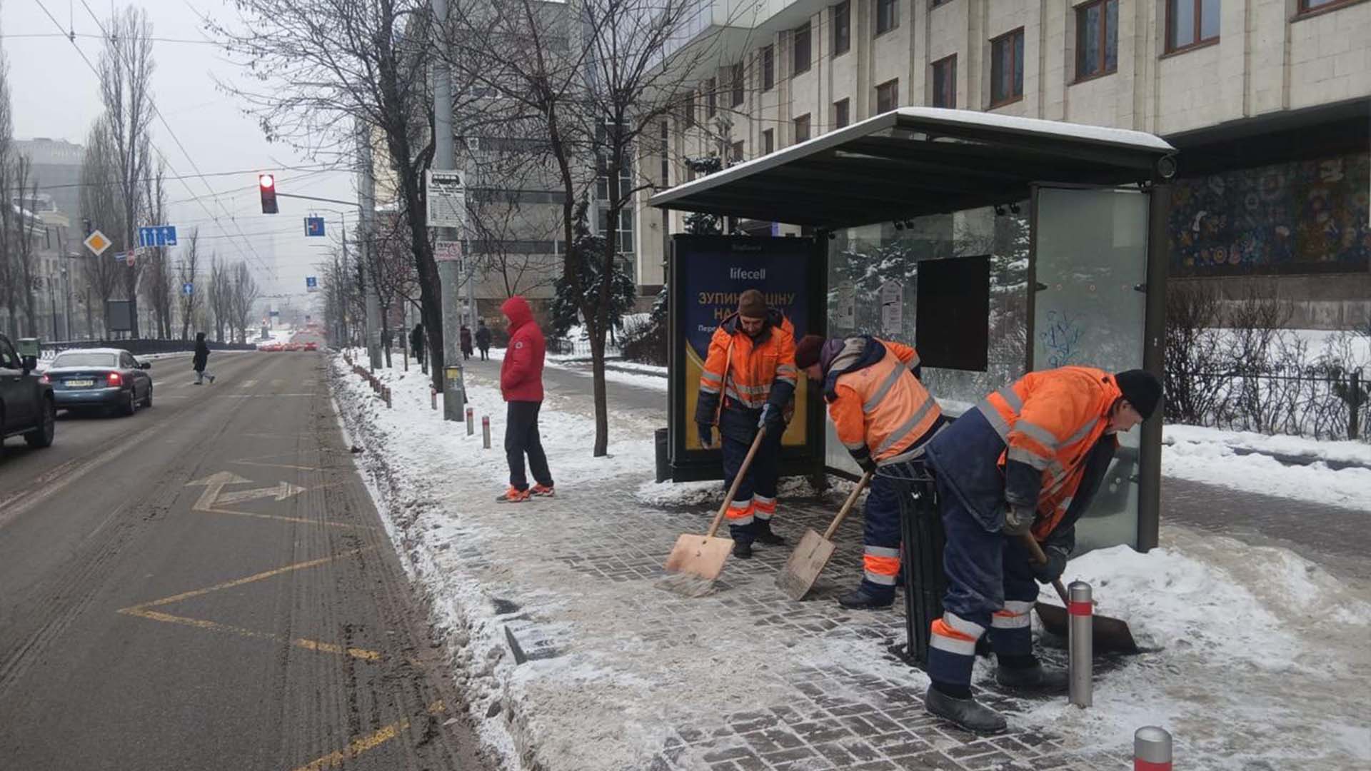 Працівники комунальної служби очищають від снігу територію біля зупинки громадського транспорту