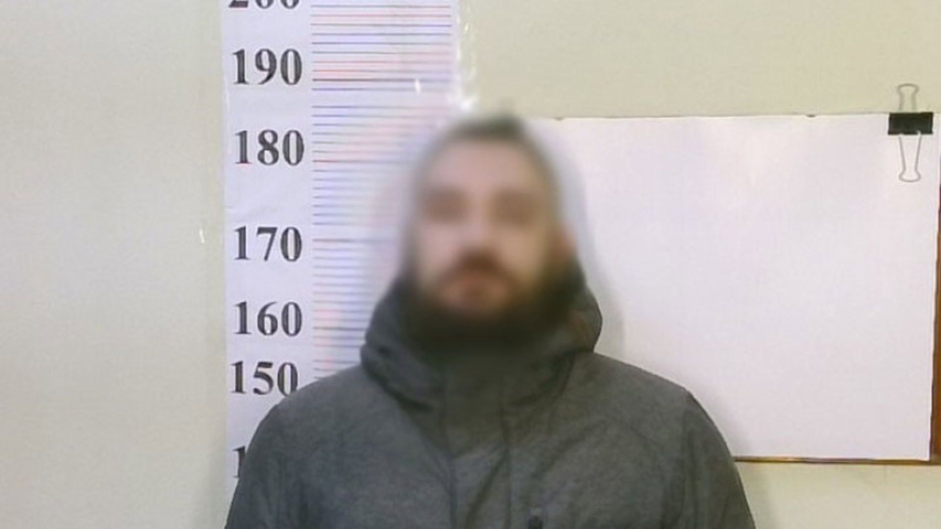 Підозрюваний біля стіни, на кій лінійка для вимірювання зросту