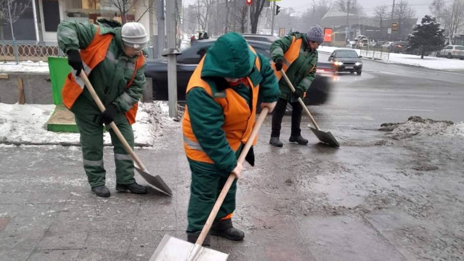 Троє комунальниць із лопатами очищають тротуар