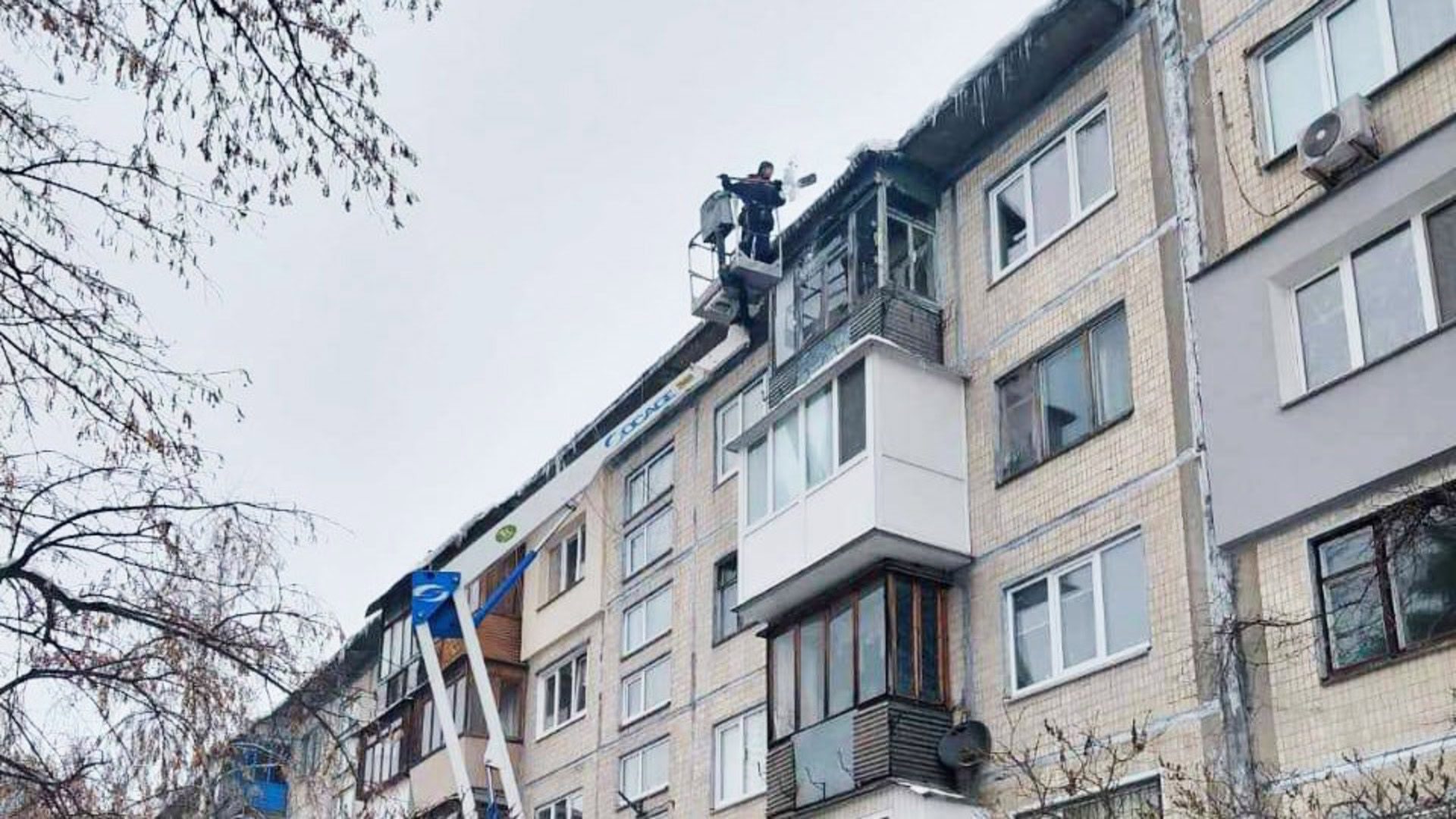 З допомогою крану очищають дах житлової будівлі від бурульок