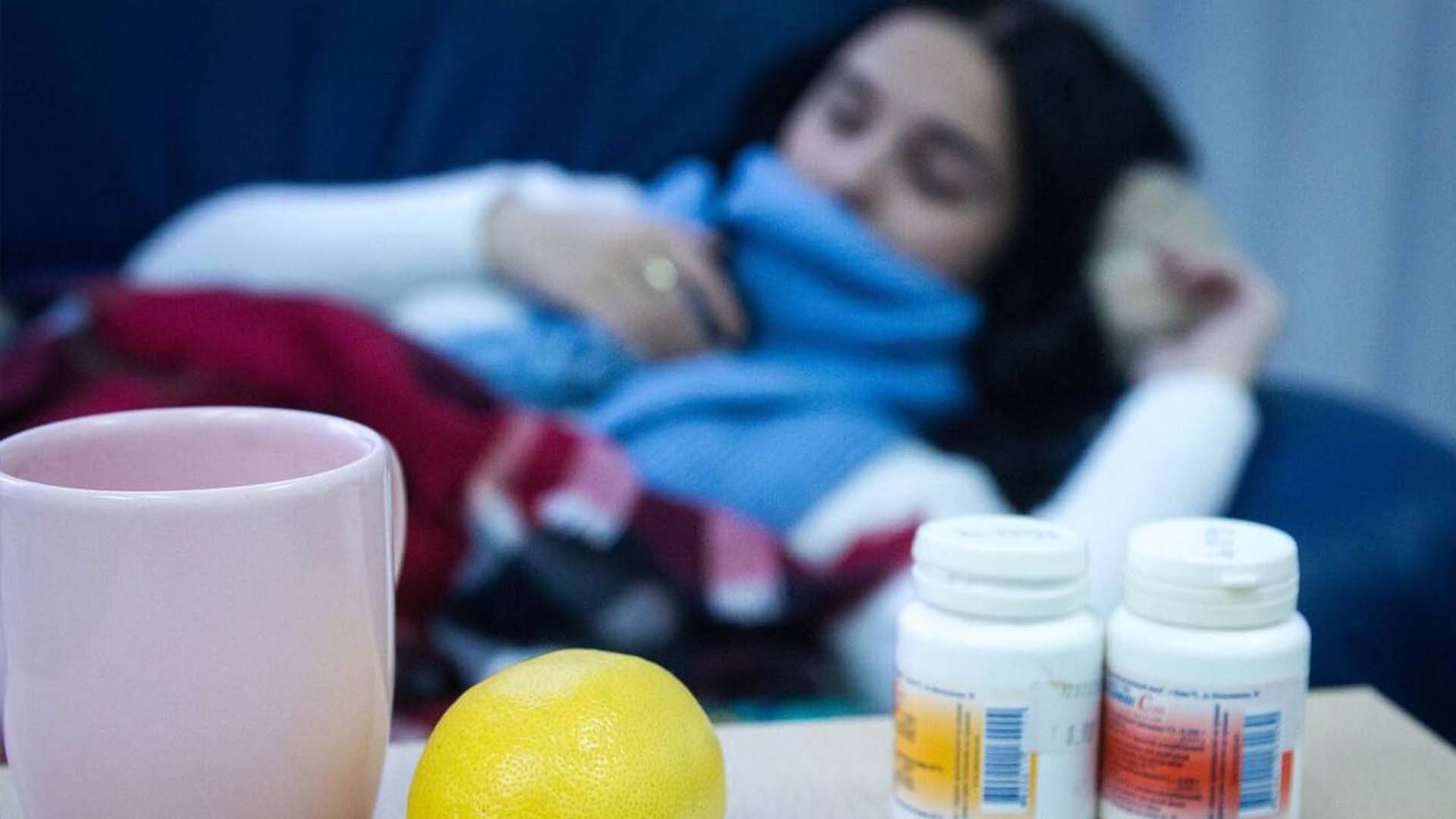 Хвора жінка на дивані, біля якої столик з ліками, лимоном та чашкою