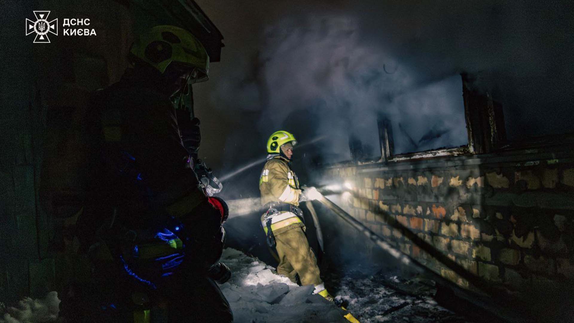Пожежник світить ліхтарем іншому пожежнику, який тягне пожежний рукав