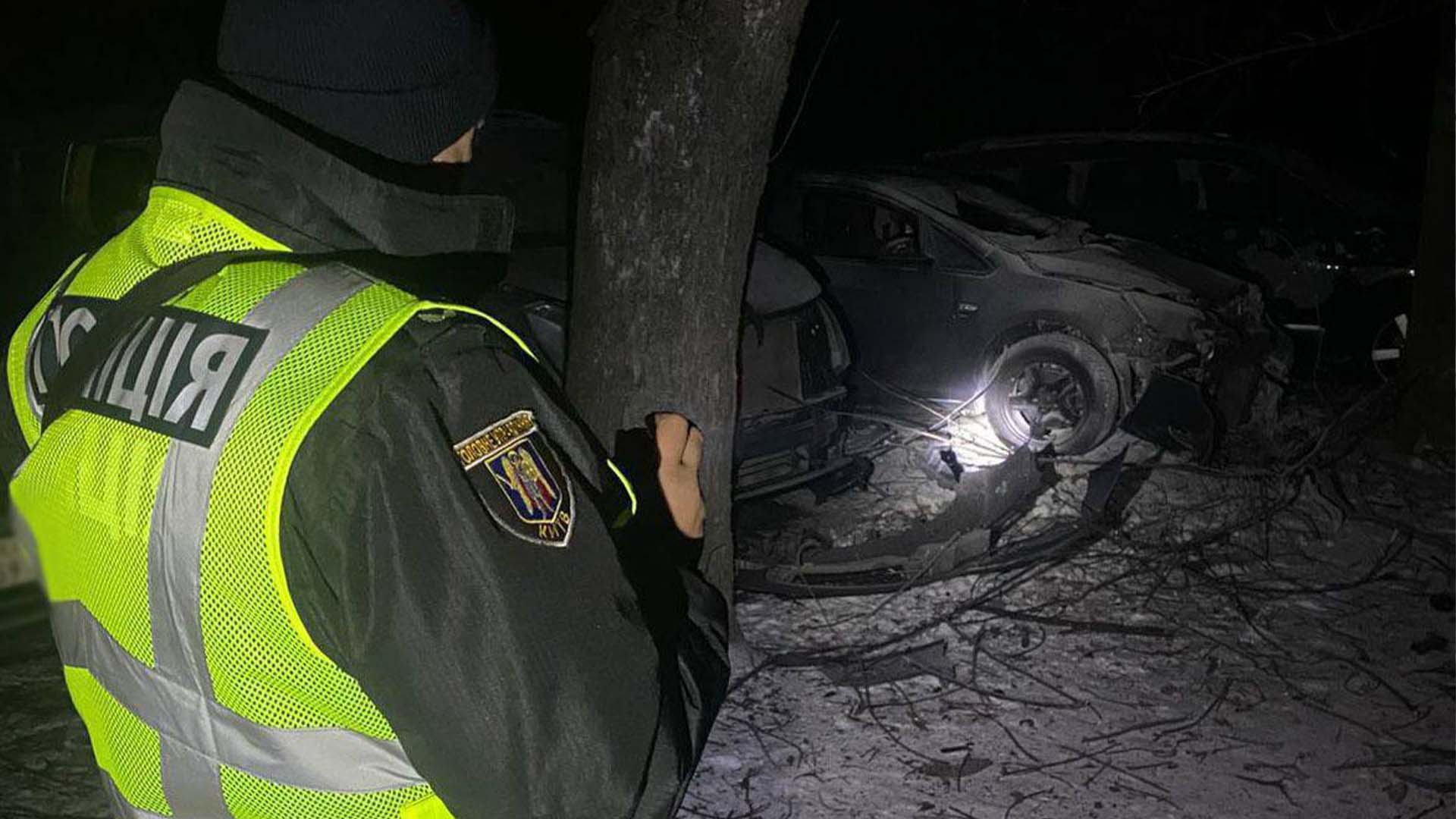 Поліцейський у нічний час біля пошкоджених автомобілів внаслідок російського удару