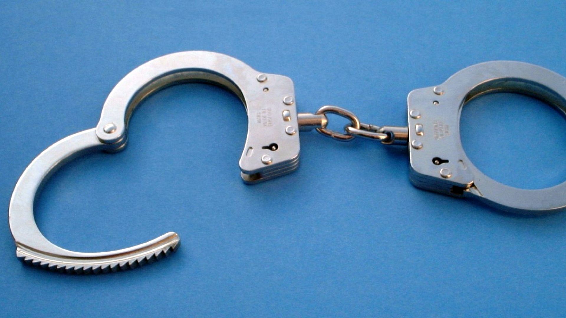 Металеві наручники на блакитному фоні — ілюстрація до кримінальної новини про засудження за розбійний напад