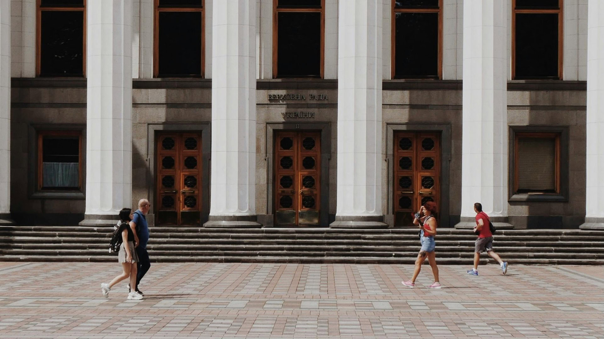 Головний вхід Верховної Ради України з масивними білими колонами та перехожими на площі перед будівлею парламенту