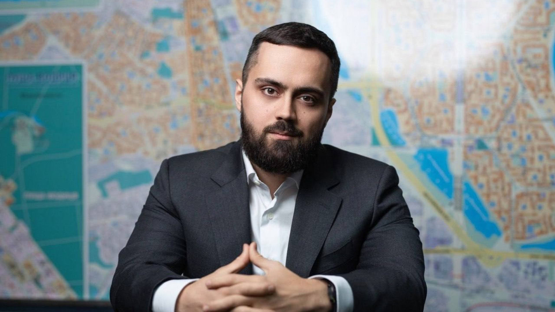 Голова Оболонської районної державної адміністрації Кирило Фесик на тлі карти міста у діловому костюмі