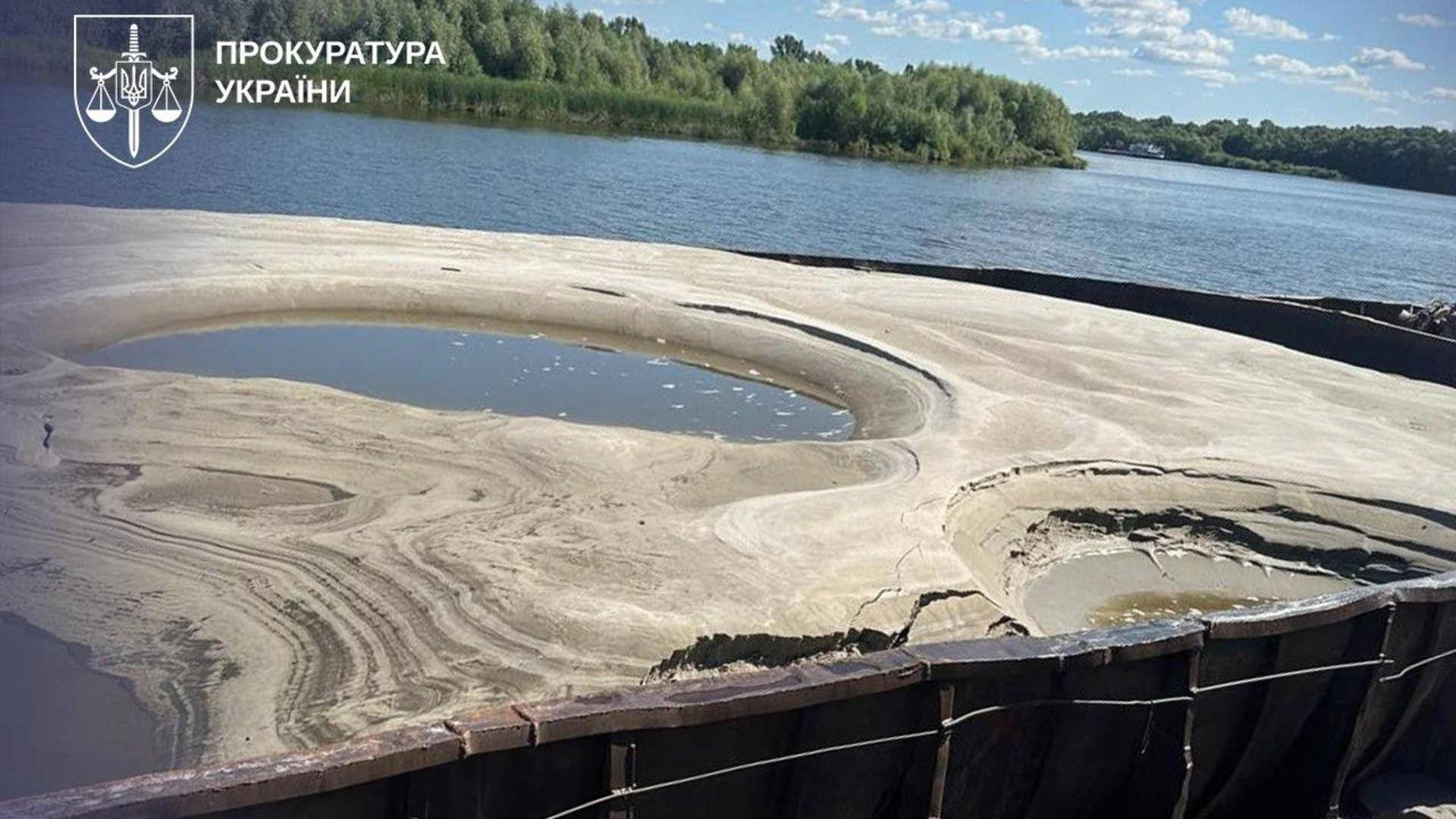 Вид зверху на баржу, заповнену піском, біля берега річки — докази у справі про незаконний видобуток