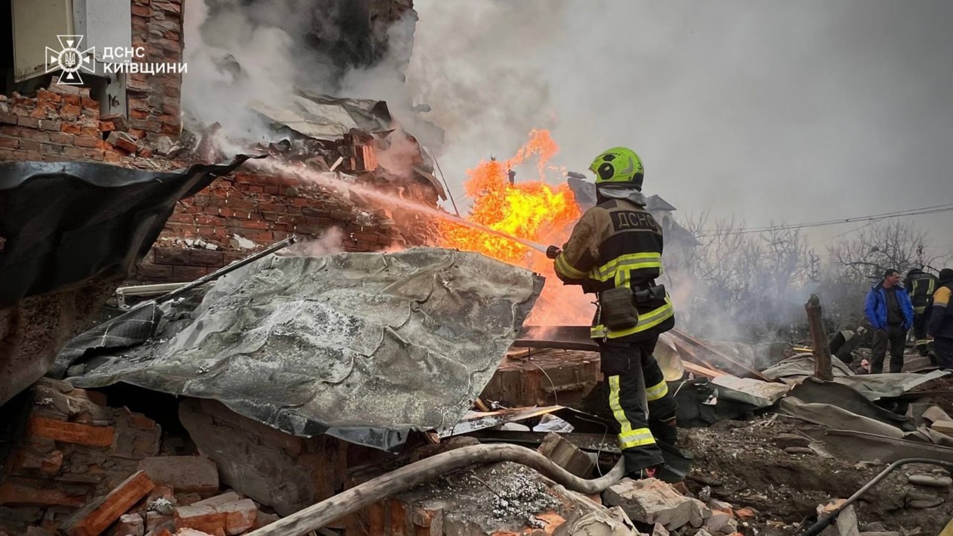 Рятувальник ДСНС Київщини у повному спорядженні спрямовує струмінь води на вогонь у зруйнованій будівлі після ракетно-дронової атаки на Київщину