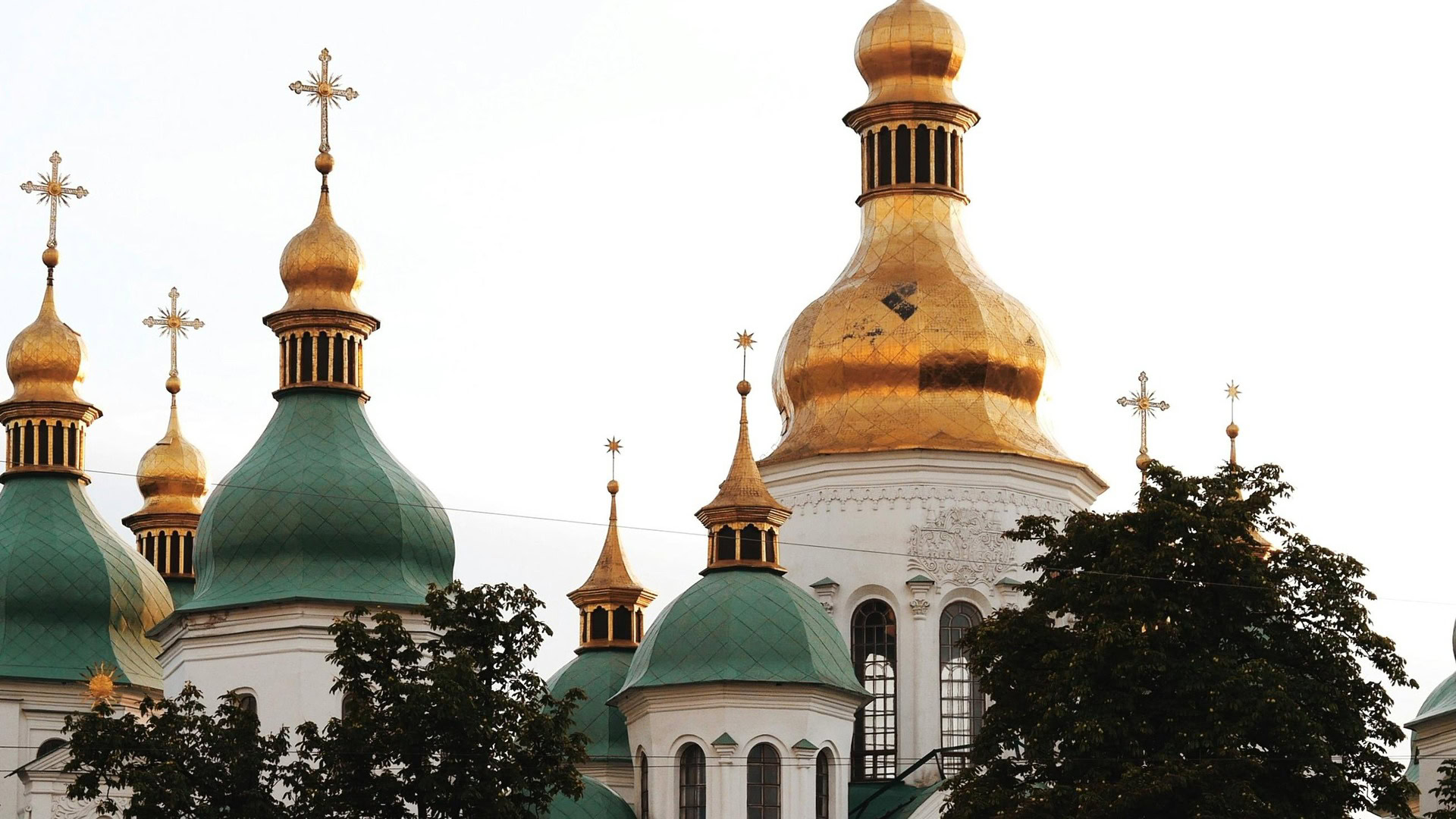 Золоті та зелені куполи з хрестами Софійського собору в Києві на тлі світлого неба