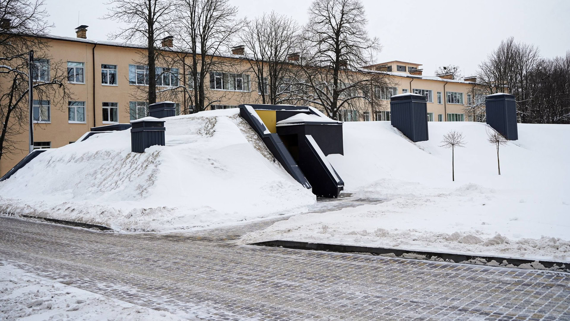 Частково заглиблене в землю протирадіаційне укриття при ліцеї Патріот у Борисполі, вхід до споруди та вентиляційні шахти, засніжена територія школи