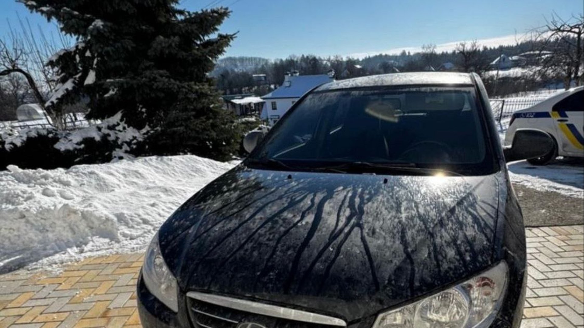 Чорний автомобіль Hyundai Elantra на засніженому подвір'ї у селі Нещерів, на задньому плані видно поліцейський автомобіль