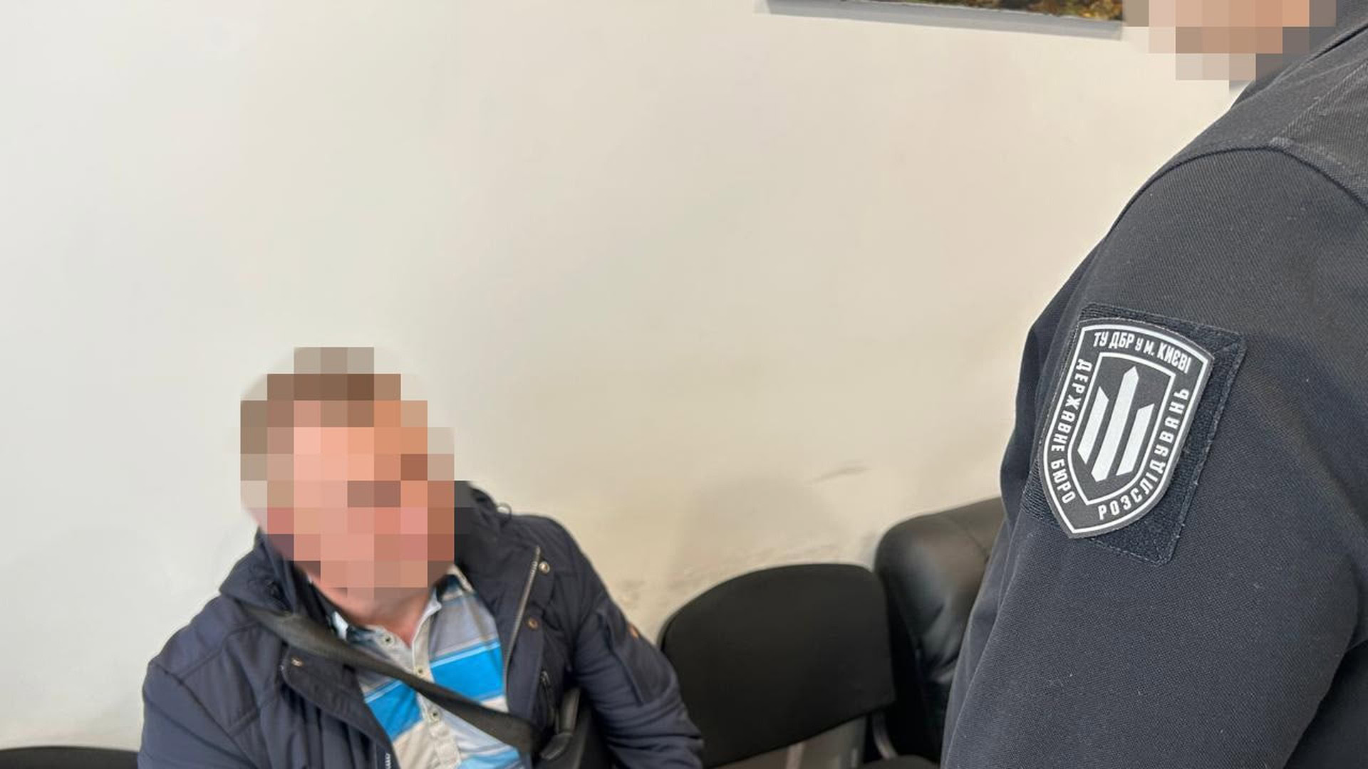 Співробітник ДБР стоїть поруч із затриманою підозрюваною у справі про розкрадання 11,5 млн грн зарплат військових НГУ