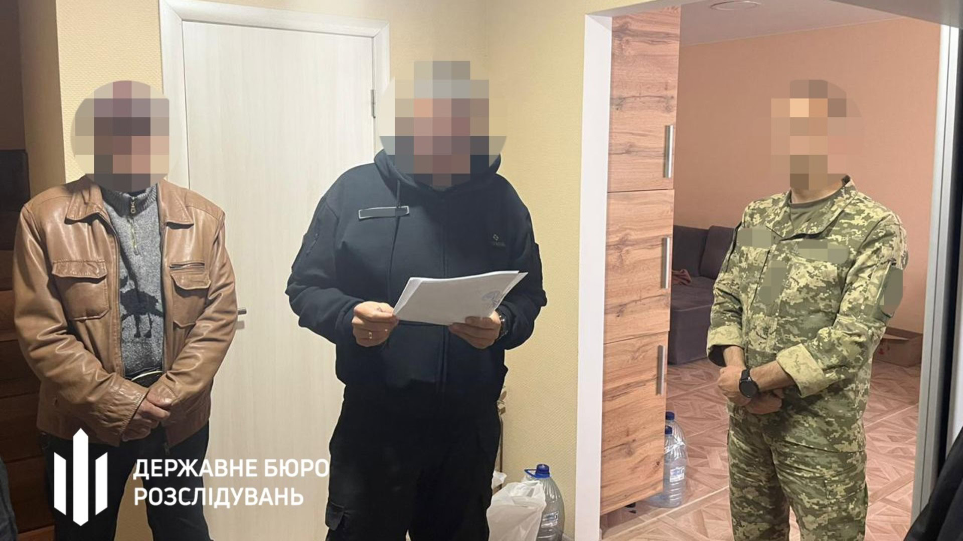 Слідчий ДБР вручає повідомлення про підозру підозрюваному — ексголові ВЛК ДПСУ, поруч стоїть військовослужбовець у камуфляжі