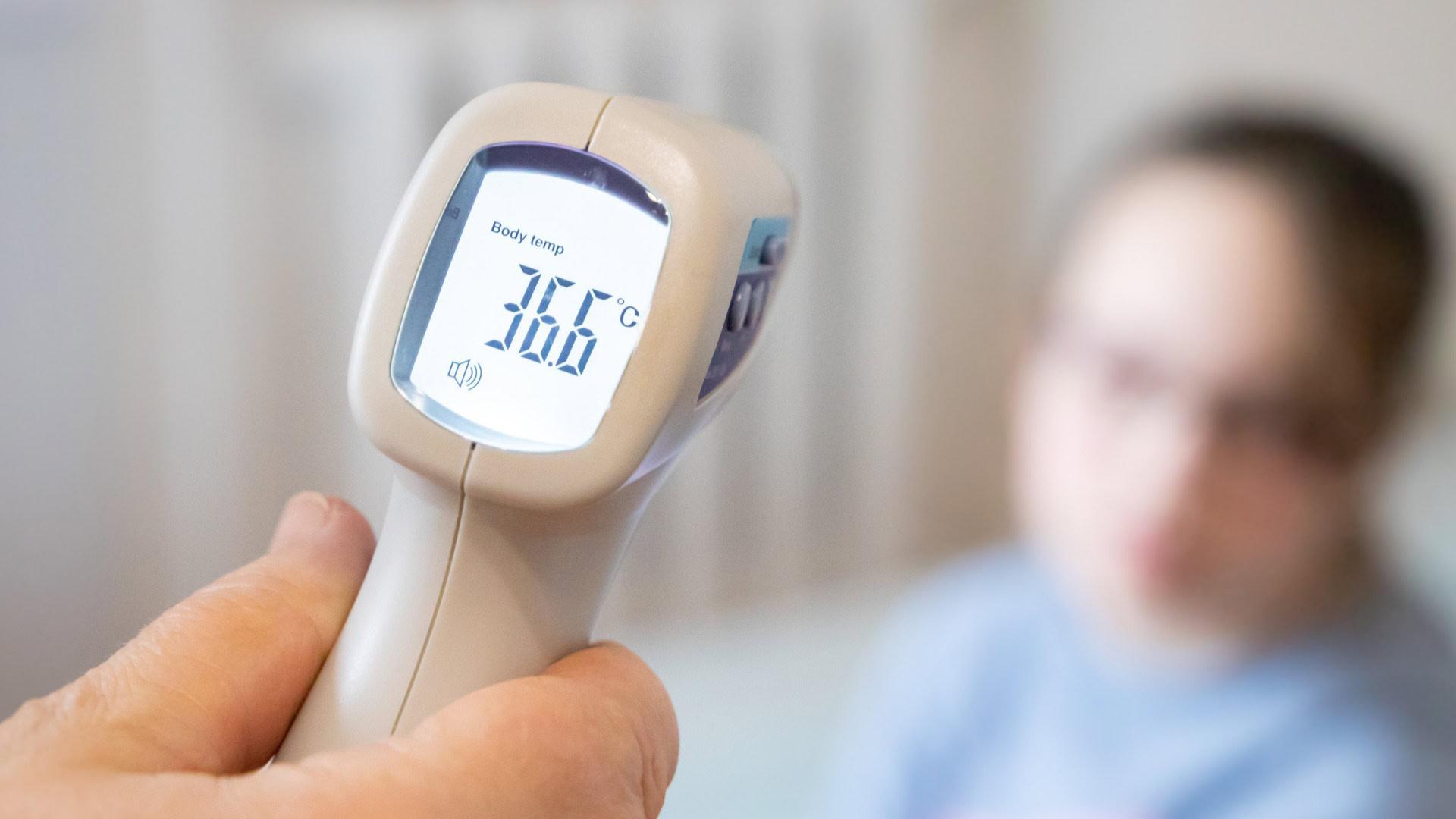 Безконтактний термометр показує температуру 36,6 градусів на фоні дитини — ілюстрація до статті про грип у Києві