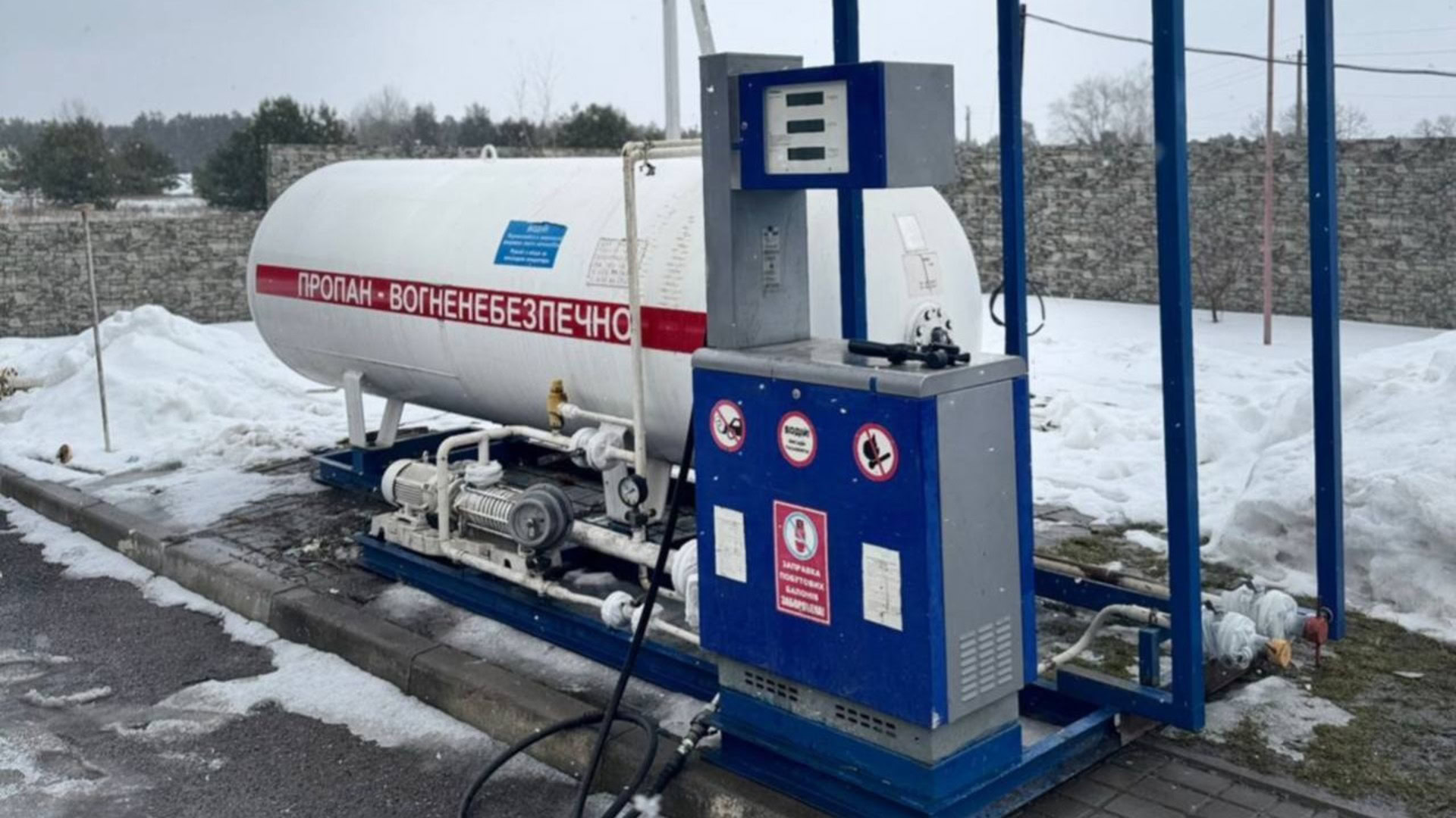 Нелегальна газова заправна станція з великим білим резервуаром пропану з написом «Вогненебезпечно» та синьою роздавальною колонкою взимку