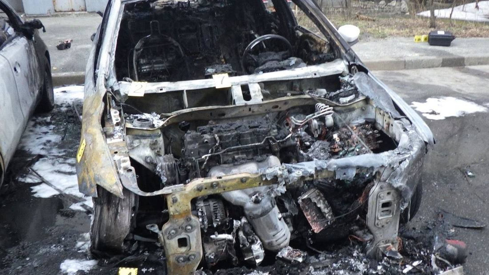 Згорілий автомобіль після підпалу в Києві, поруч пошкоджена сусідня машина, на місці працюють криміналісти