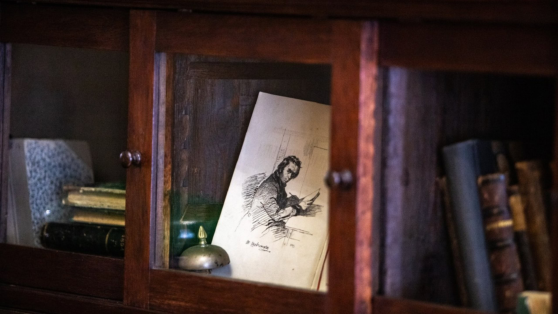 Дерев'яна вітрина з книгами та чорно-білим малюнком людини за письмовим столом — експонат до ювілею Шевченківської премії