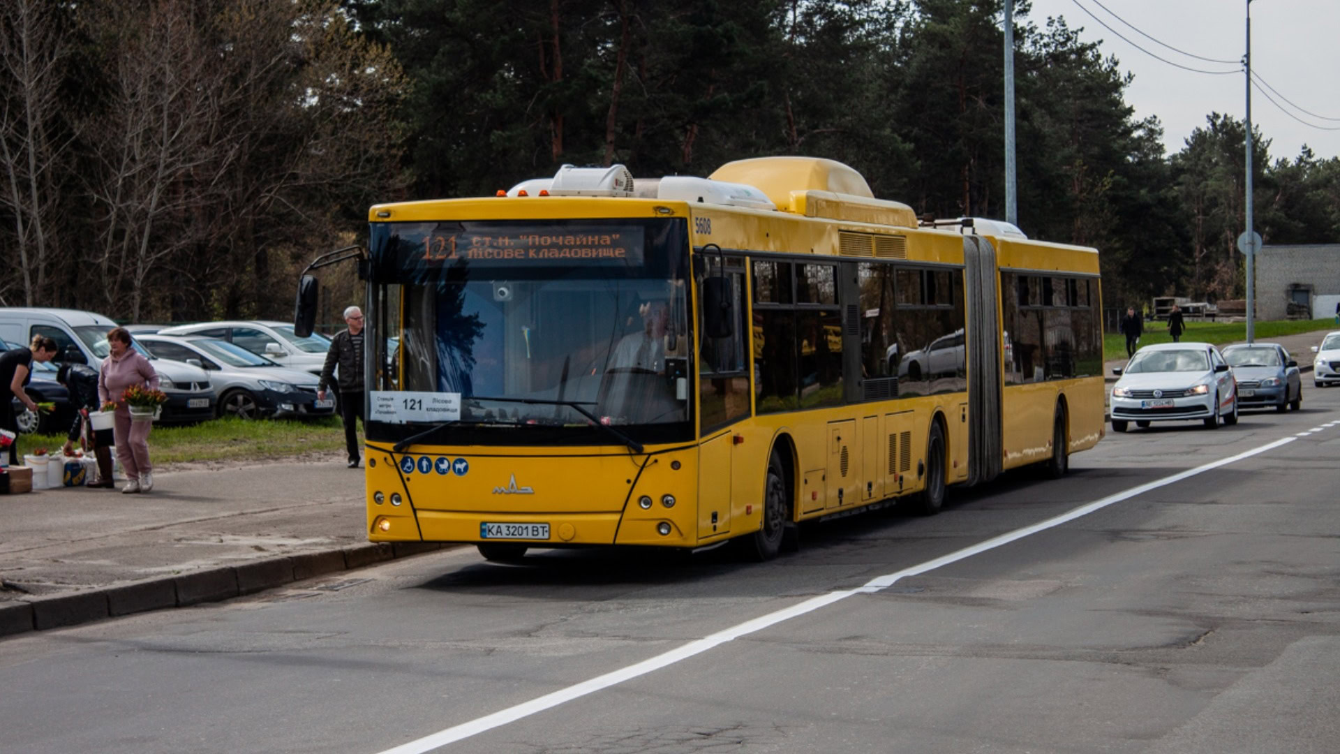 Жовтий зчленований автобус МАЗ маршруту 121 на вулиці Києва, на табло напис «ст. м. Почайна — Лісове кладовище»