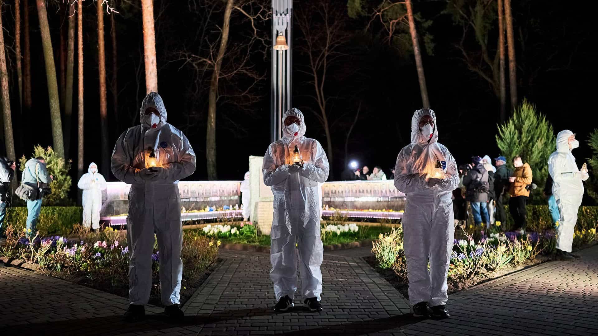 Учасники у захисних костюмах тримають свічки пам'яті біля меморіалу ліквідаторів Чорнобиля у Славутичі вночі на 26 квітня 2026 року