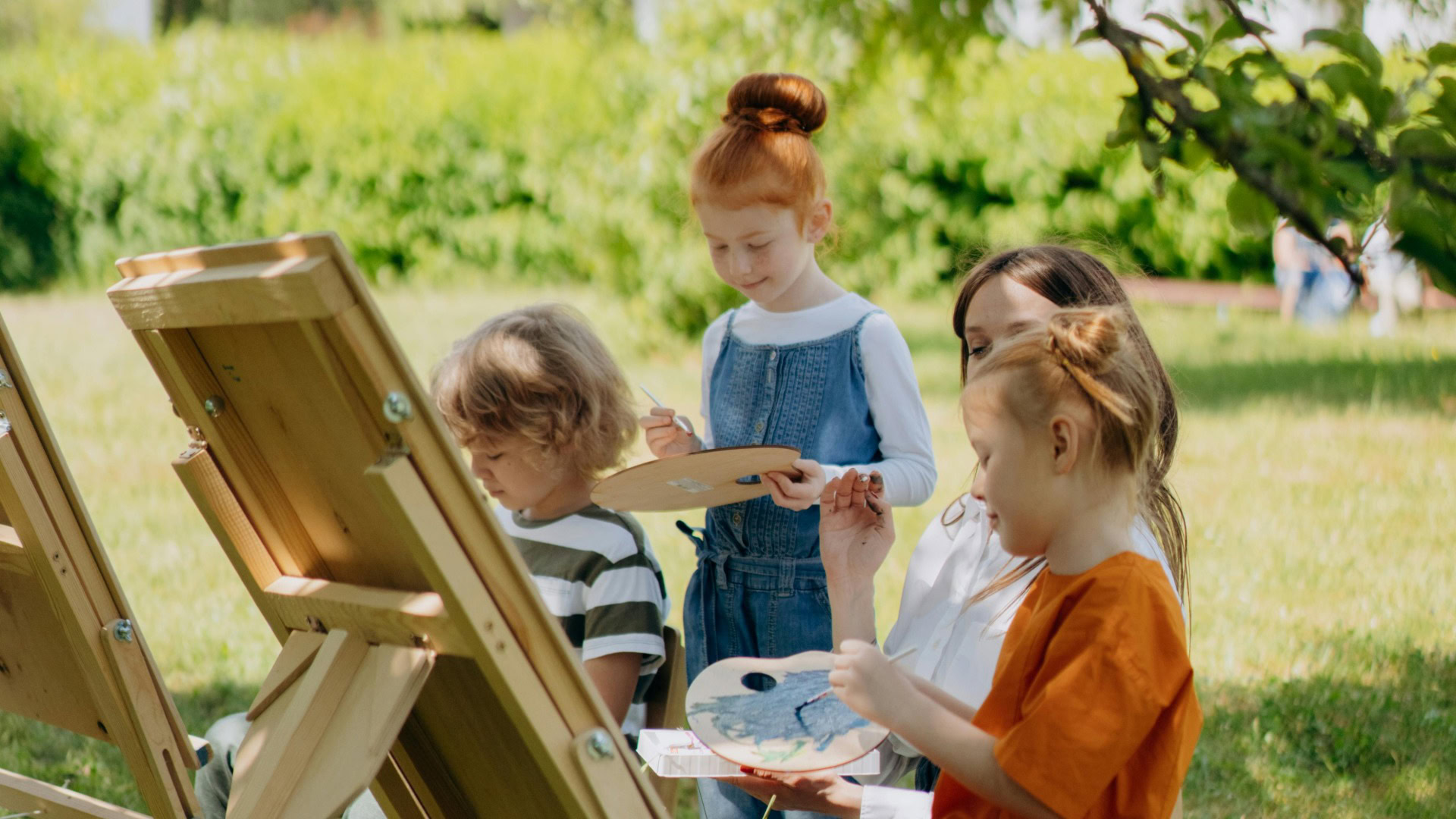 Троє дітей малюють фарбами на мольберті у парку в сонячний весняний день