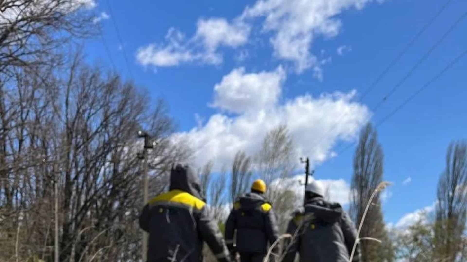 Три енергетики ДТЕК у спецодязі йдуть вздовж лінії електропередачі серед дерев під час ліквідації аварій після негоди на Київщині у квітні 2026 року
