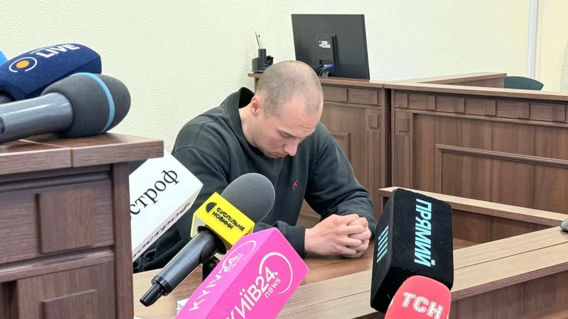 Патрульний поліцейський сидить у залі суду оточений мікрофонами телеканалів під час засідання щодо теракту в Голосіївському районі Києва
