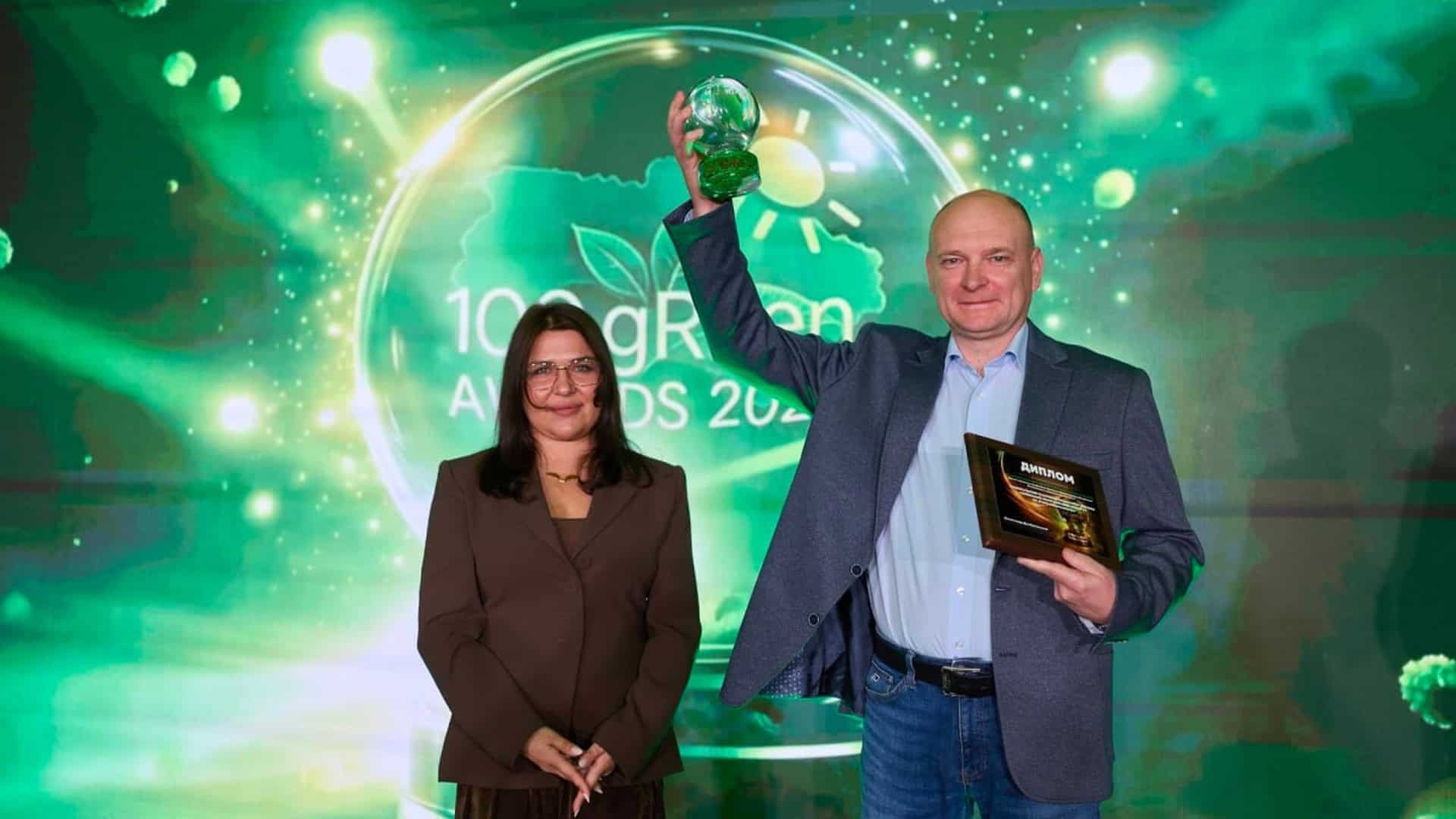 Доцент НН ІЕЕ КПІ Леонід Лістовщик піднімає скляний кубок нагороди 100 gREen AWARD-2025 на сцені поруч з ведучою заходу