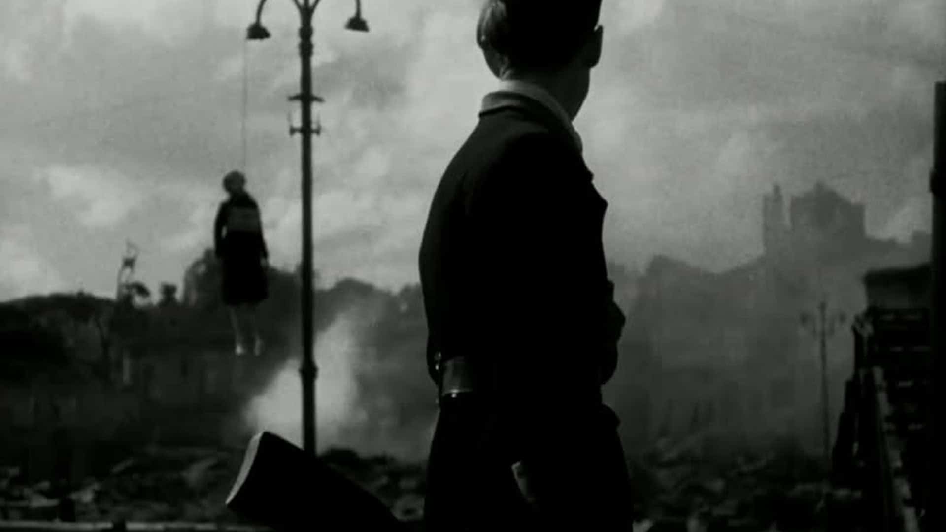 Чорно-білий кадр із фільму «Нескорені» (1944): силует солдата з рушницею на тлі зруйнованого міста і диму, чоловік у формі стоїть спиною до глядача