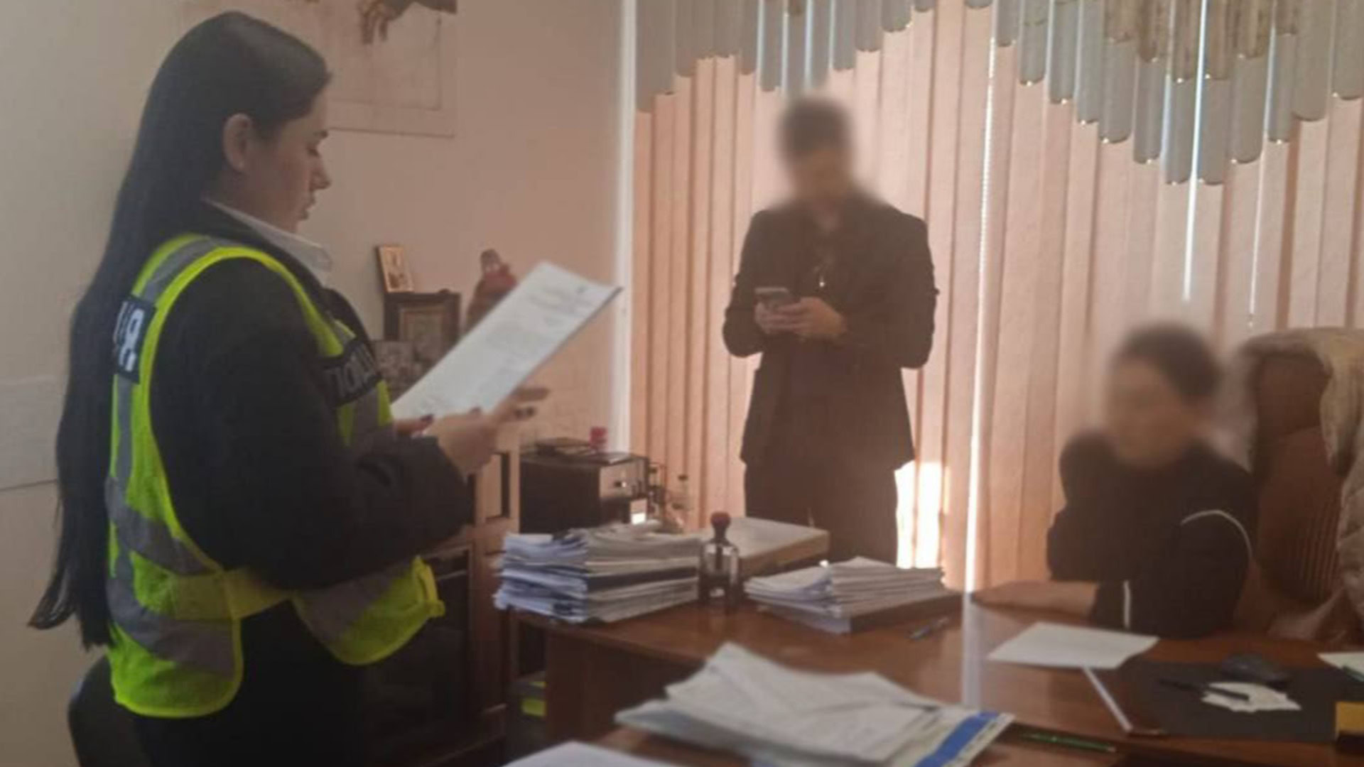 Слідча у жовтому жилеті зачитує підозру у нотаріальній конторі під час розслідування шахрайства з нерухомістю