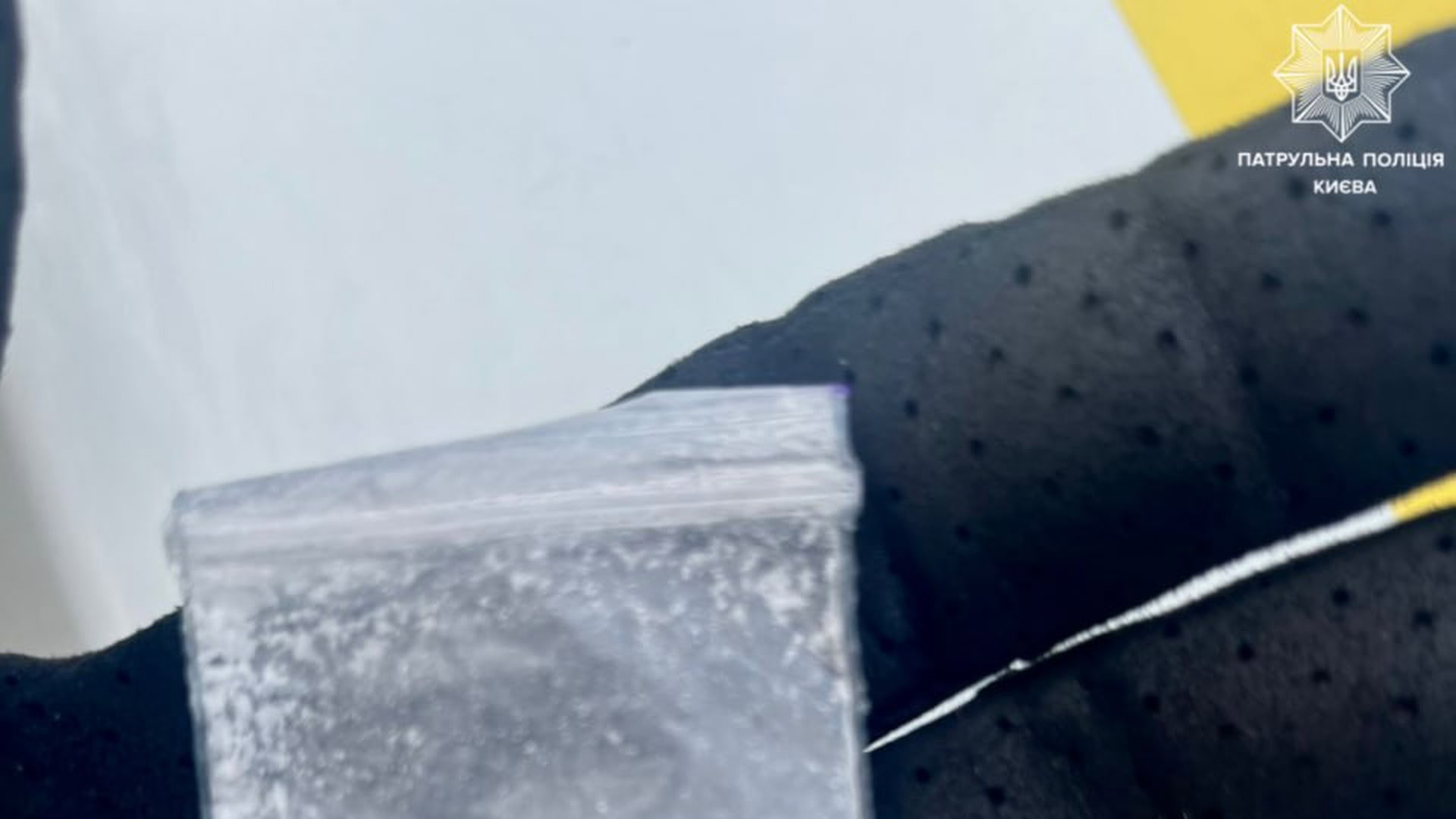 Рука поліцейського в чорній рукавичці тримає прозорий пакетик з білою речовиною схожою на наркотик