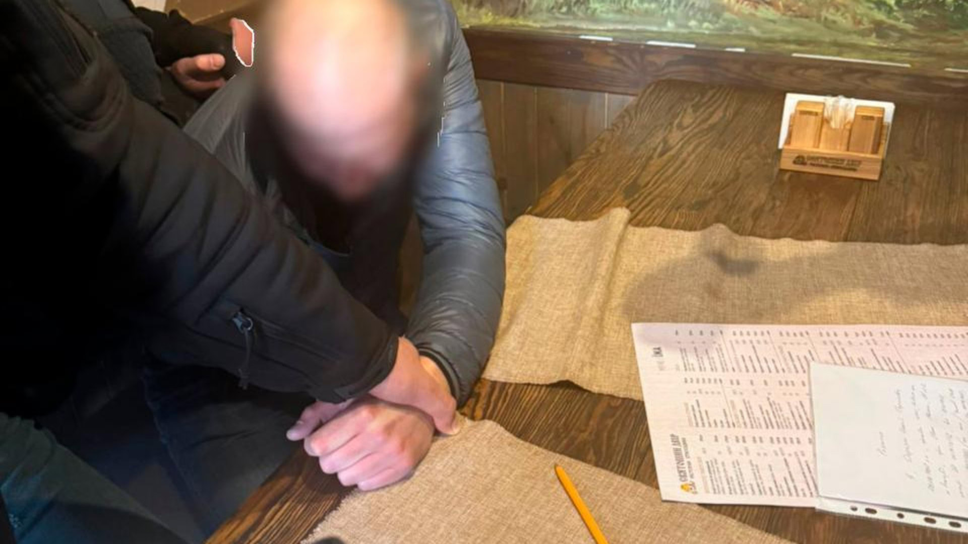 Затриманий посадовець Укрзалізниці сидить із зав'язаними руками під час обшуку, на столі документи та олівець