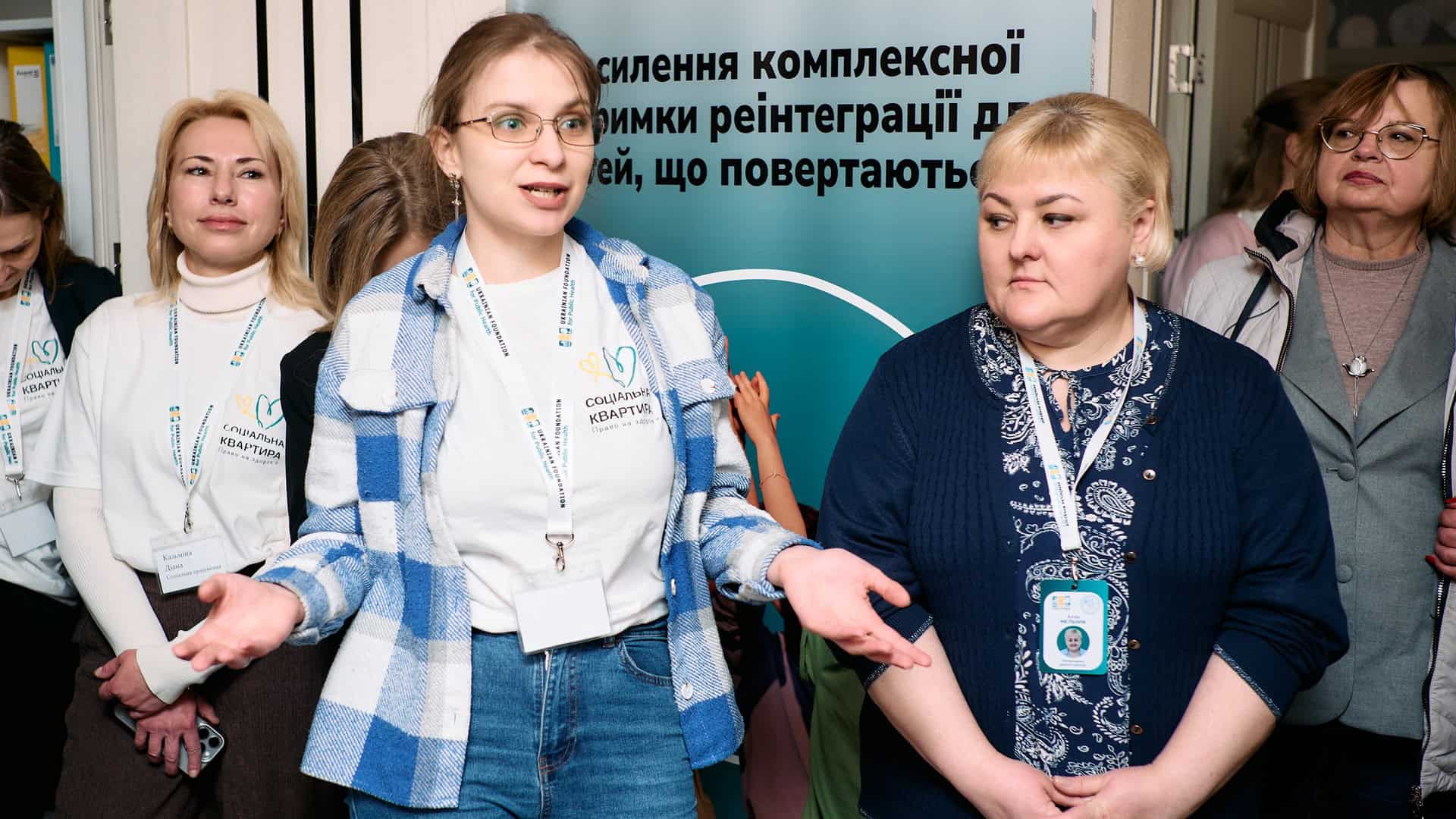 Учасниці відкриття соціальної квартири у Києві для юнаків з окупованих територій — жінки з бейджами «Соціальна квартира» на тлі банеру проєкту Bring Kids Back UA