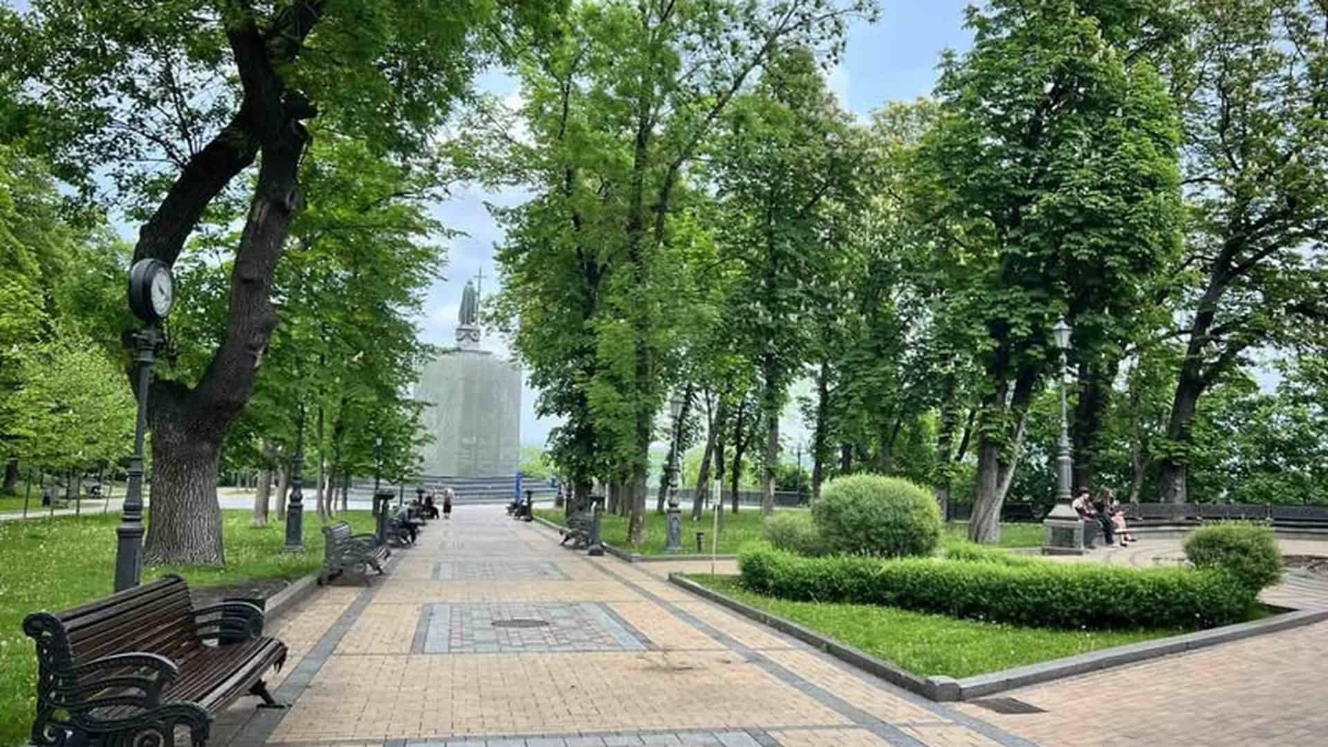Алея парку «Володимирська гірка» в Києві з лавочками, деревами та пам'ятником князю Володимиру на задньому плані
