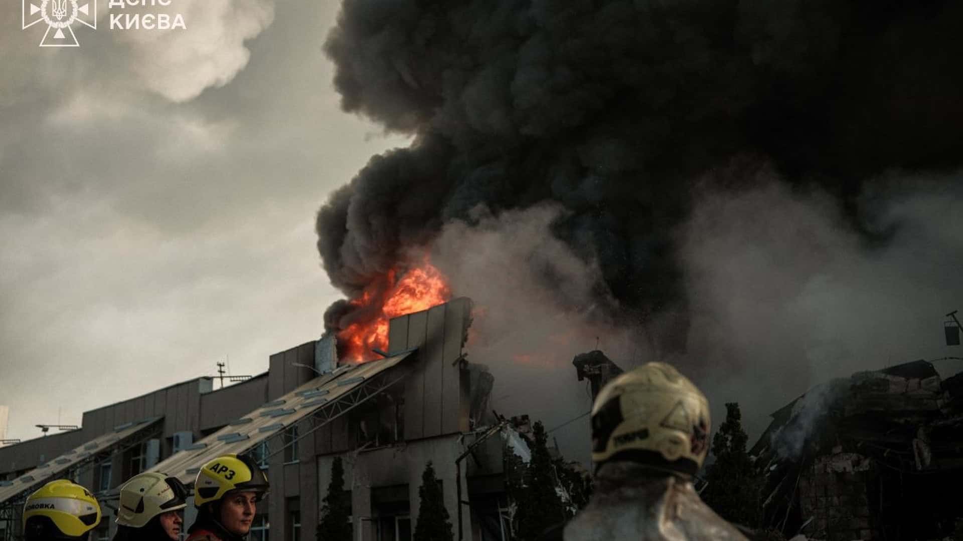 Пожежники ДСНС на тлі полум'я та густого диму гасять пожежу в пошкодженій будівлі після удару по Києву