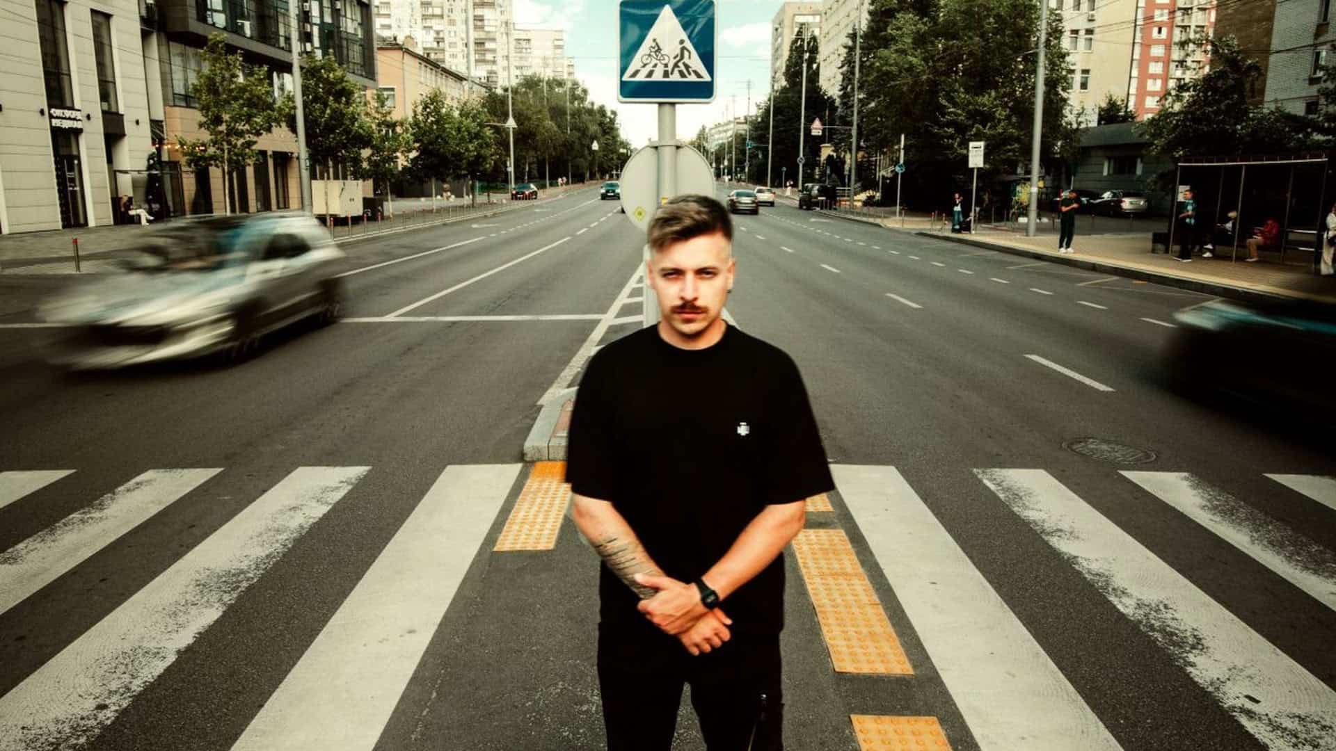 DJ Grim у чорному одязі стоїть на пішохідному переході на широкій вулиці Києва, презентуючи альбом «НЕ35ОРИМІ»