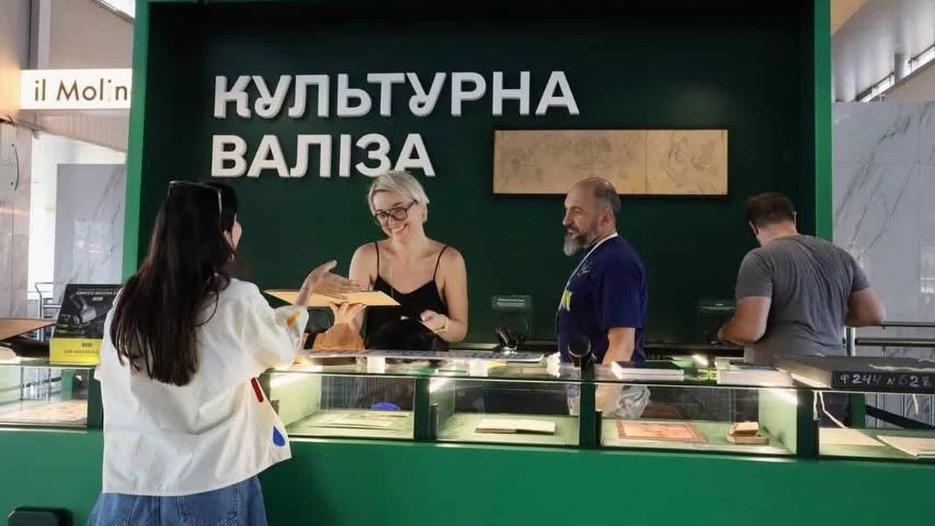 Відвідувачка отримує артефакт на виставці «Культурна валіза» на київському вокзалі, куратори за стійкою серед вітрин з експонатами