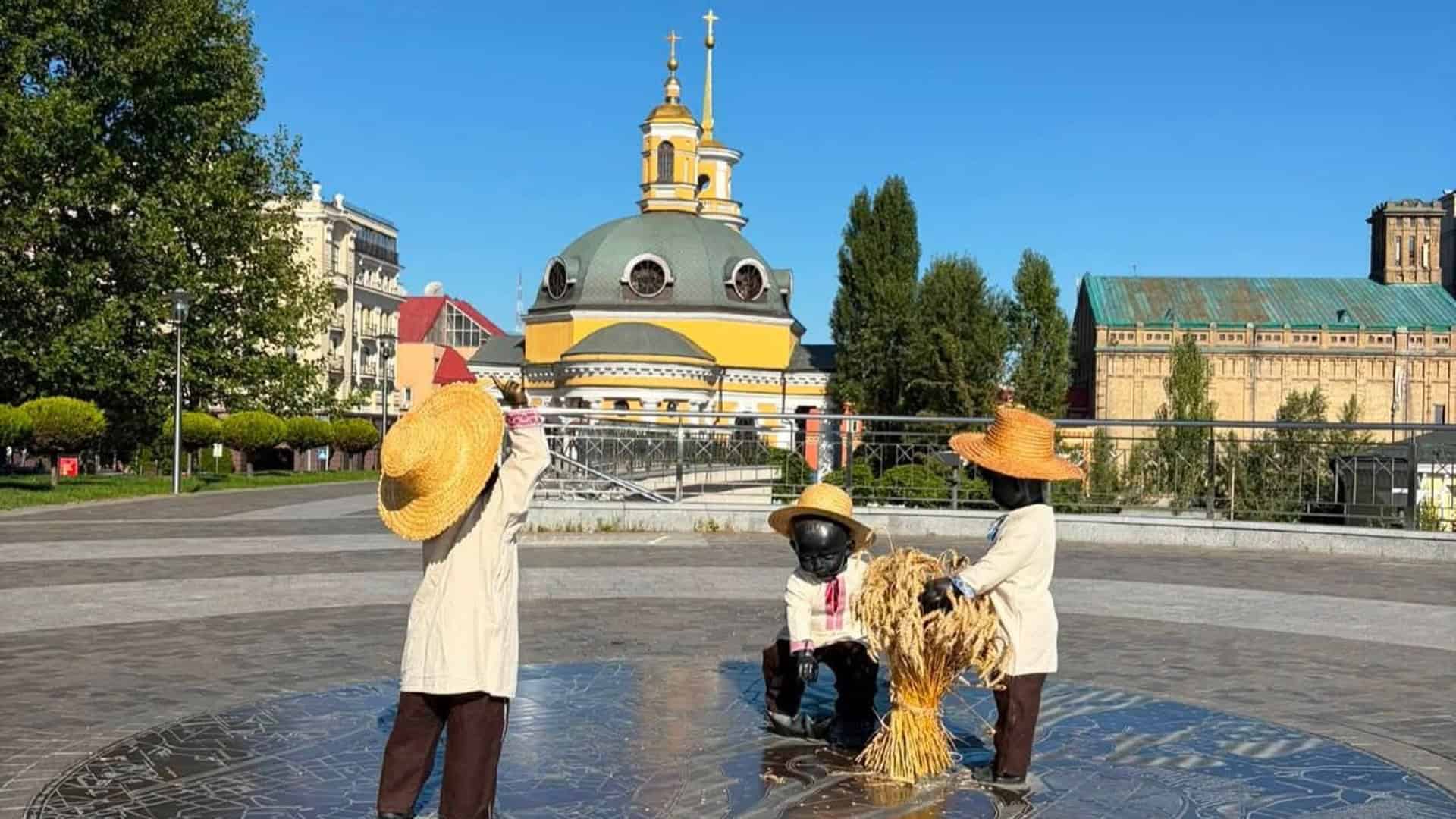 Скульптурна композиція «Малюки-засновники» на Поштовій площі в Києві одягнена в солом’яні капелюхи та вишиванки до свята Обжинок, на тлі церкви