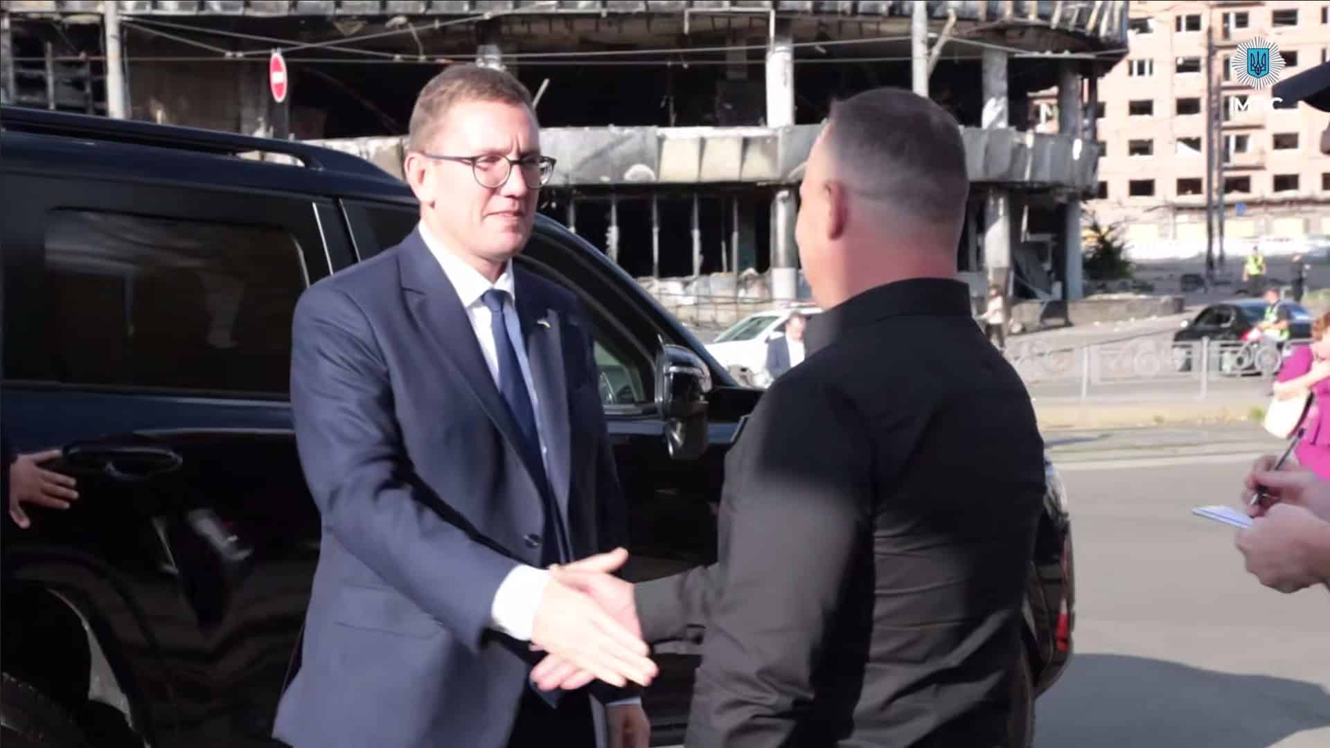 Прем’єр Естонії Крістен Міхал тисне руку голові ДСНС Андрію Данику на тлі зруйнованого торгового центру на Лук’янівці в Києві