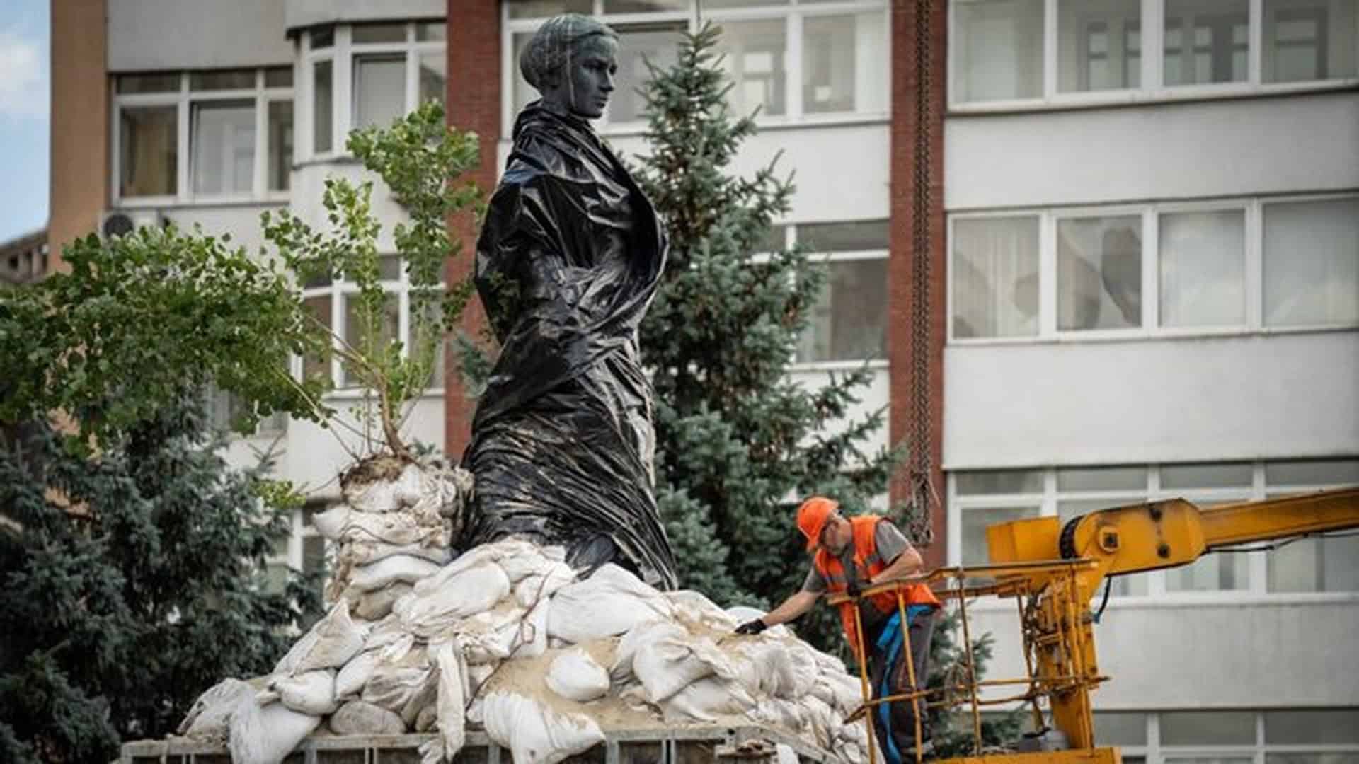 Пам'ятник Лесі Українці в мішках з піском, робітник у робочому одязі демонтує захисну конструкцію за допомогою підіймальної техніки