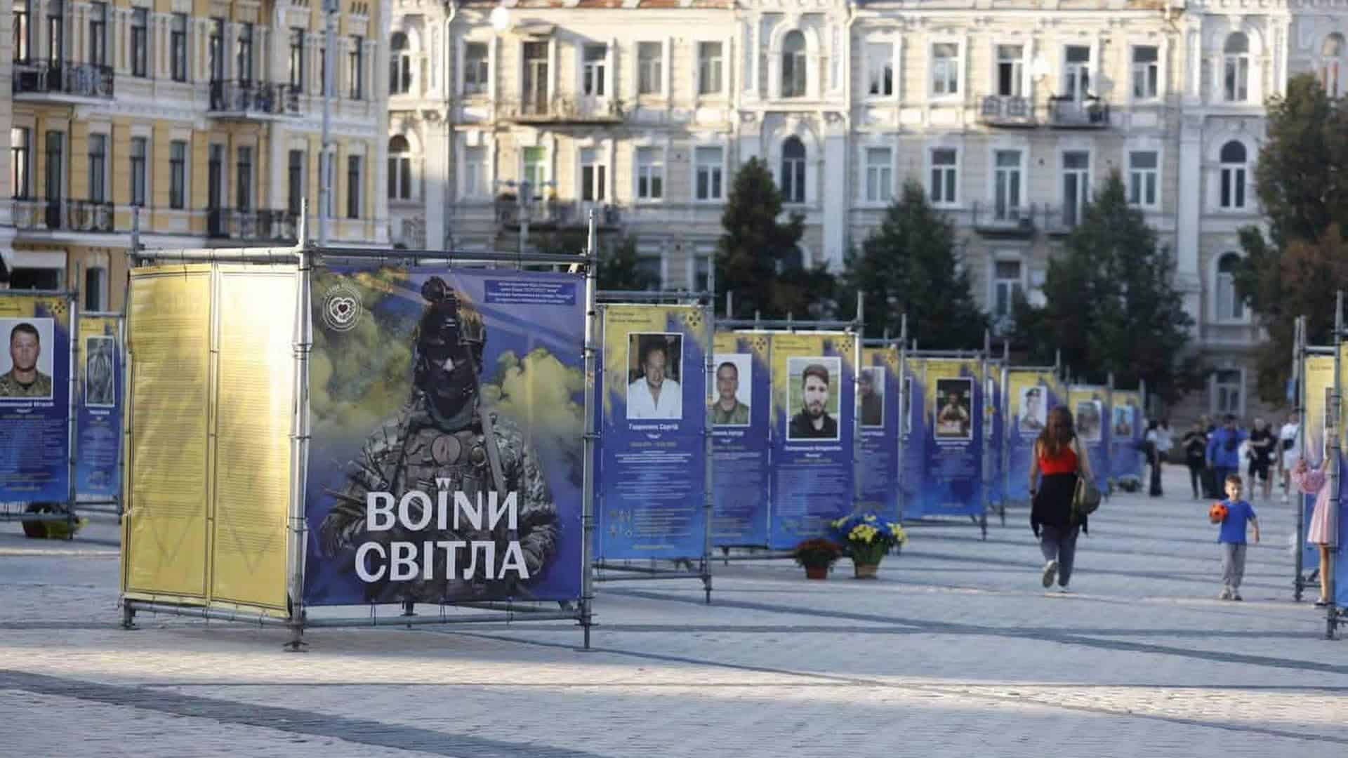 Стенди виставки «Воїни світла» з портретами полеглих захисників на Софійській площі в Києві, перехожі поруч