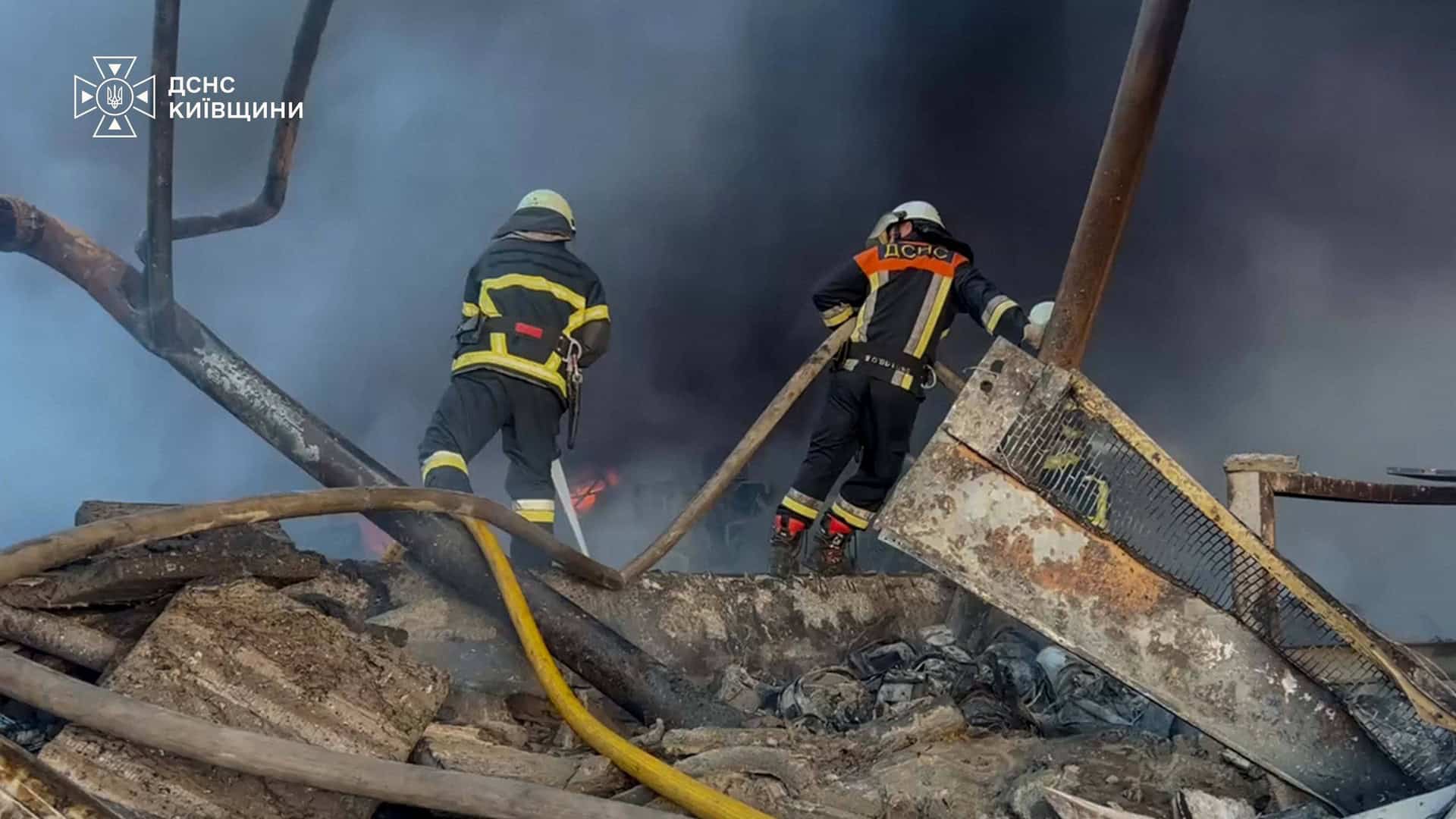 Двоє рятувальників ДСНС працюють серед обгорілих металевих конструкцій на місці пожежі на Київщині