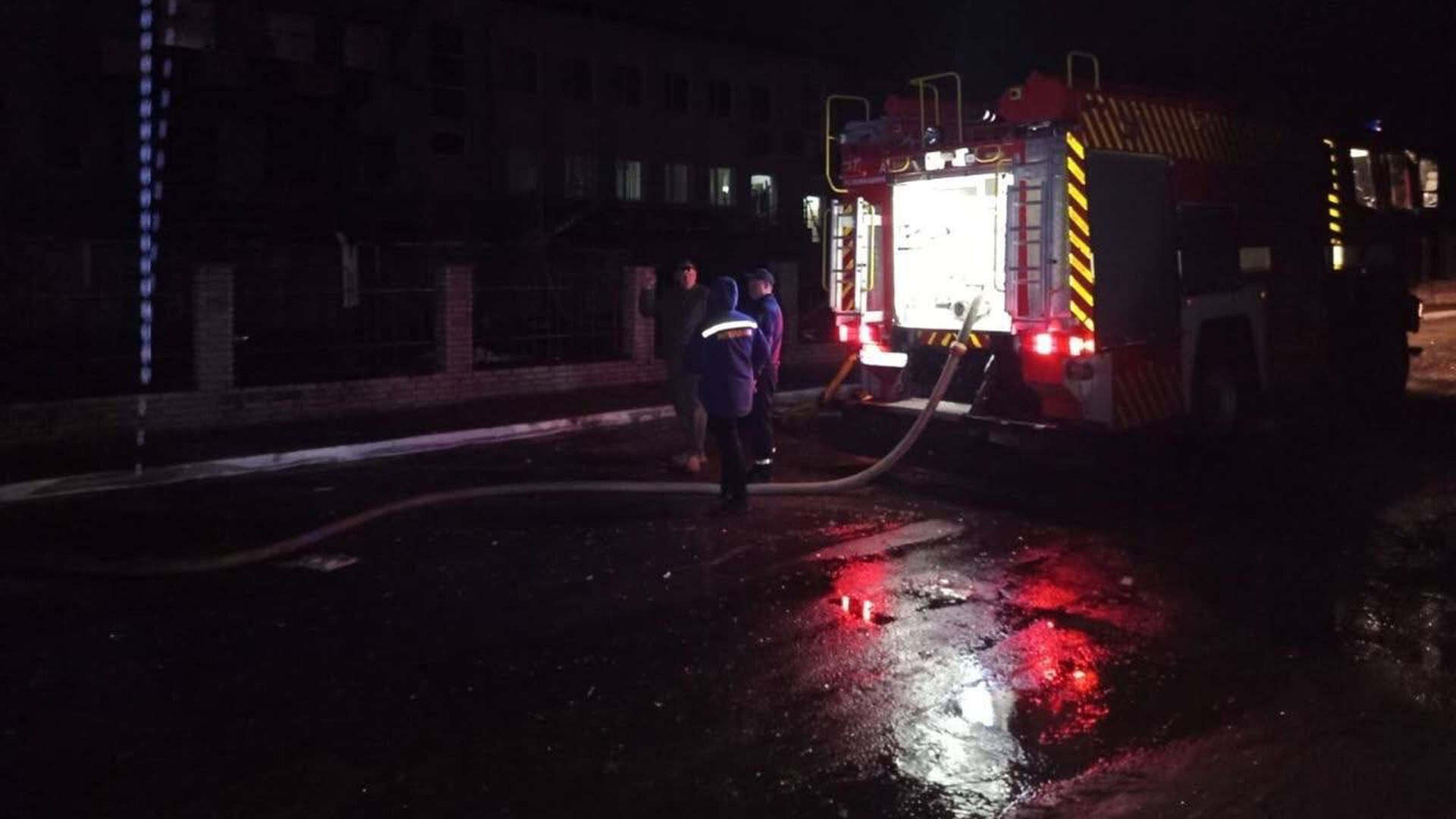 Пожежна машина ДСНС із розгорнутим рукавом стоїть біля огорожі багатоповерхової будівлі, поруч рятувальники, ніч