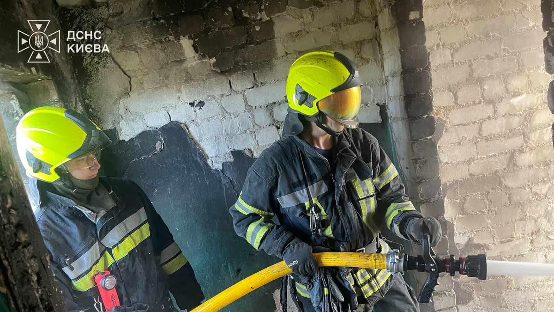 Двоє рятувальників ДСНС у захисному спорядженні з пожежним рукавом усередині пошкодженої будівлі після атаки на Київ